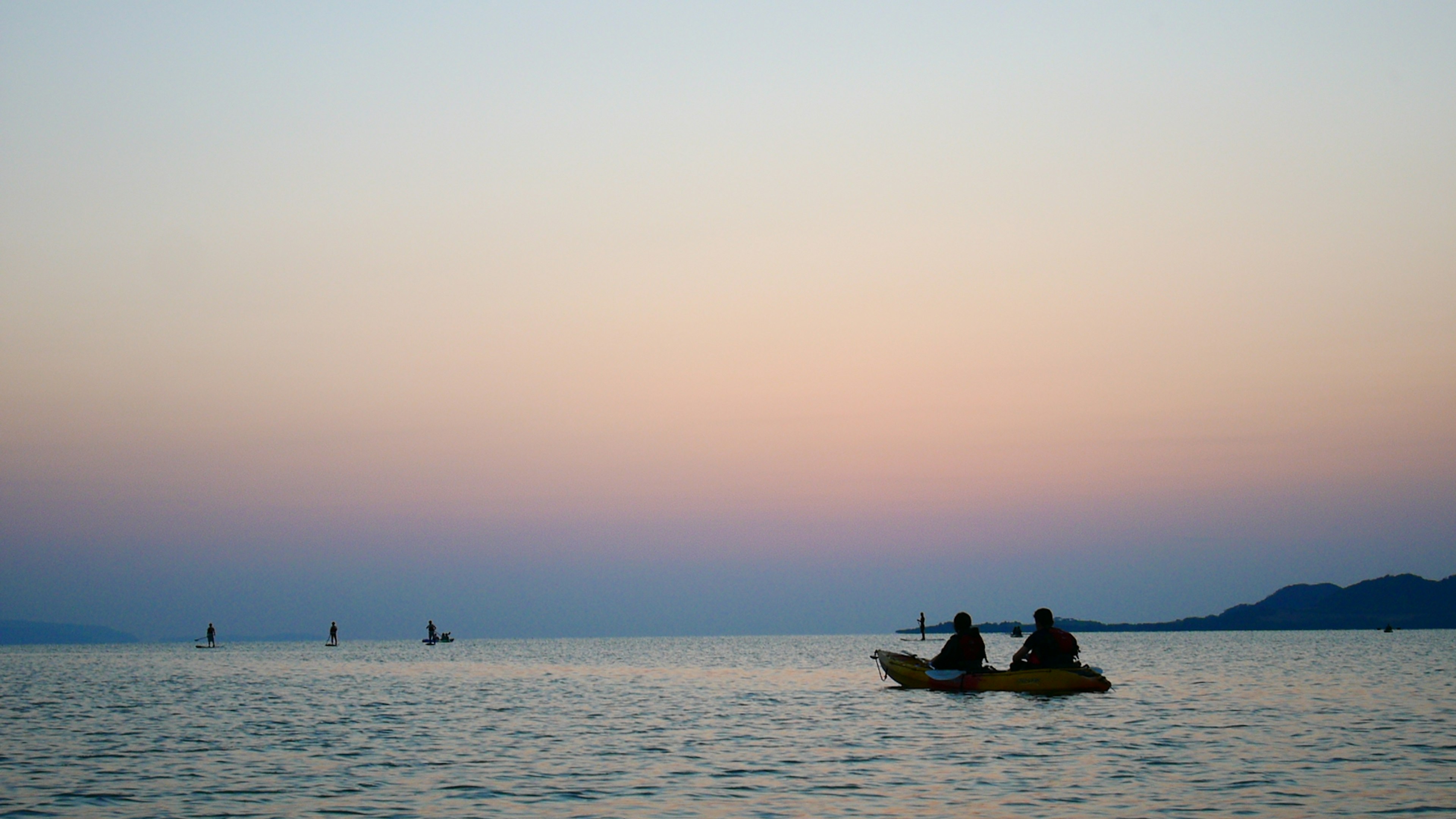 Two people kayaking on a serene sea at sunset