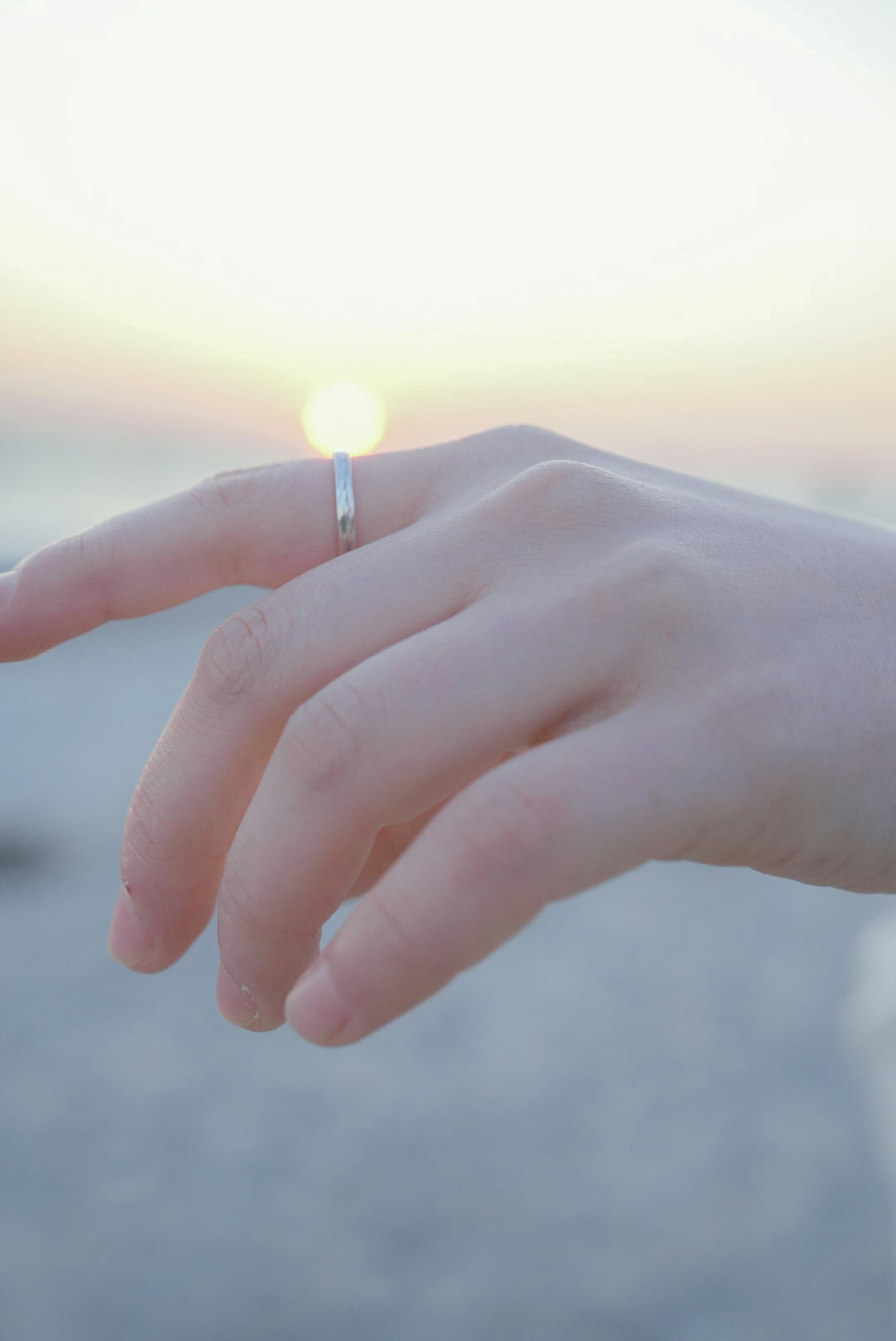 Mano con anillo alcanzando el atardecer