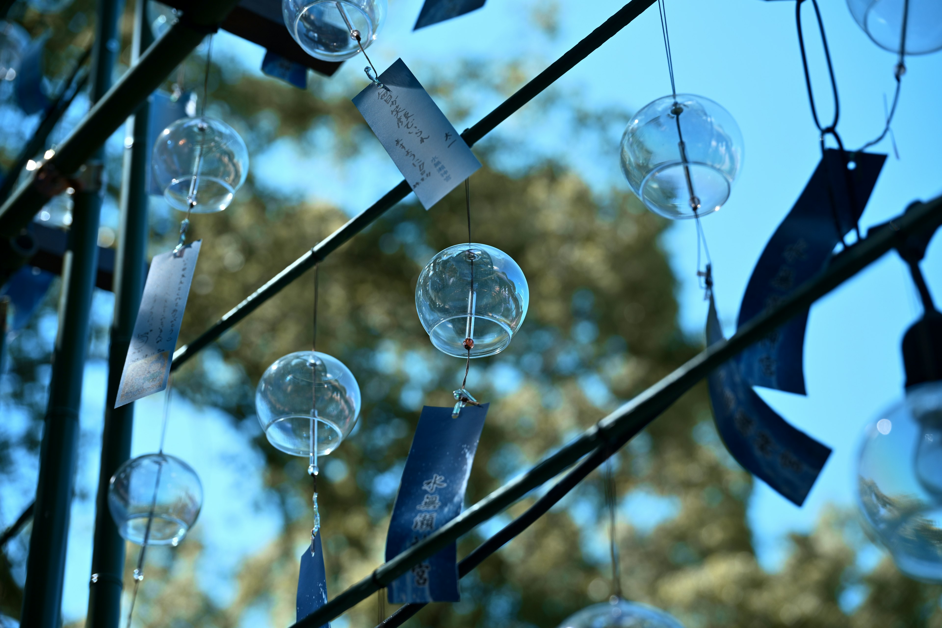 Installazione artistica di campane a vento appese sotto un cielo blu con vetro trasparente e nastri blu