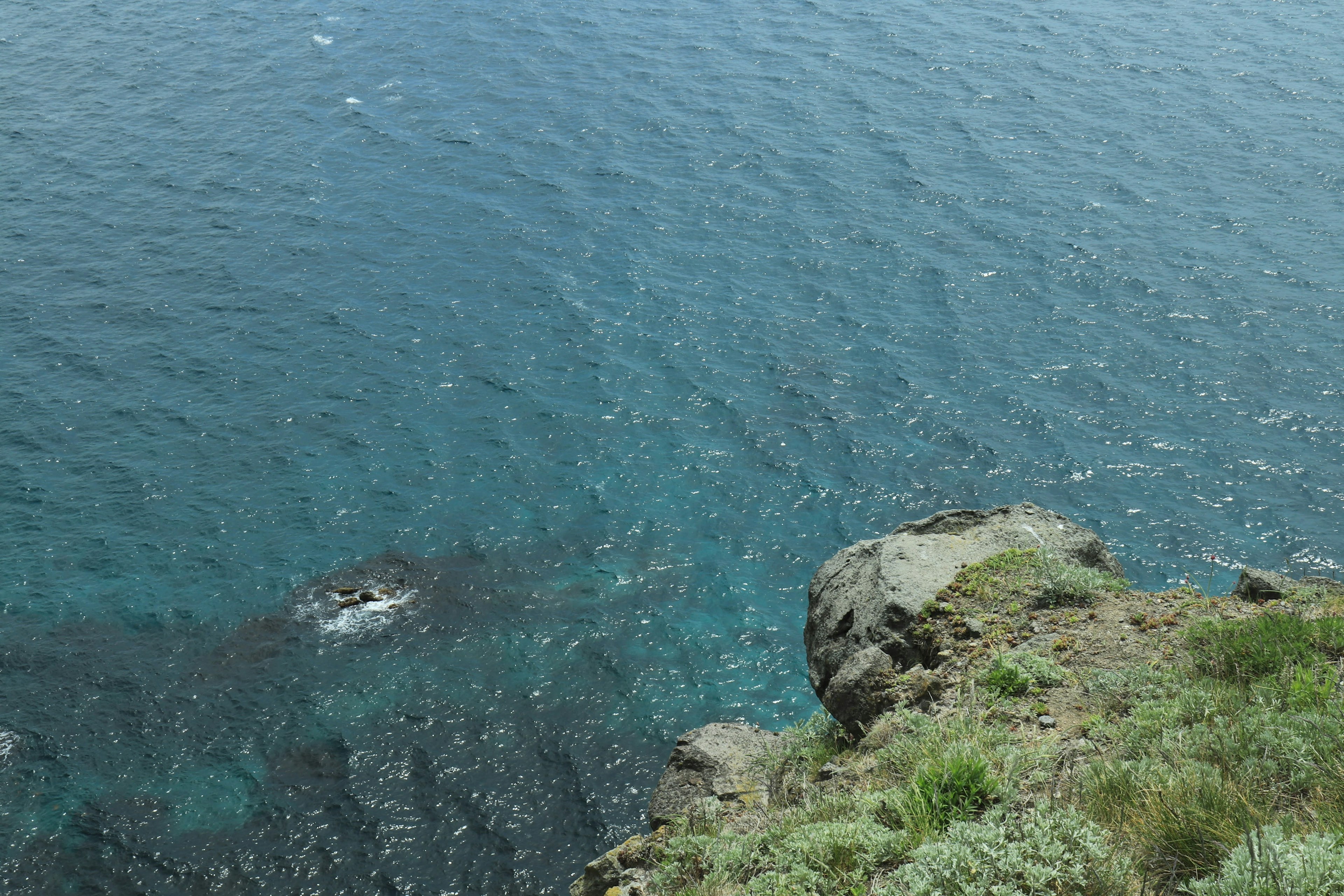 Pemandangan dari tebing yang menghadap laut biru dan rumput hijau