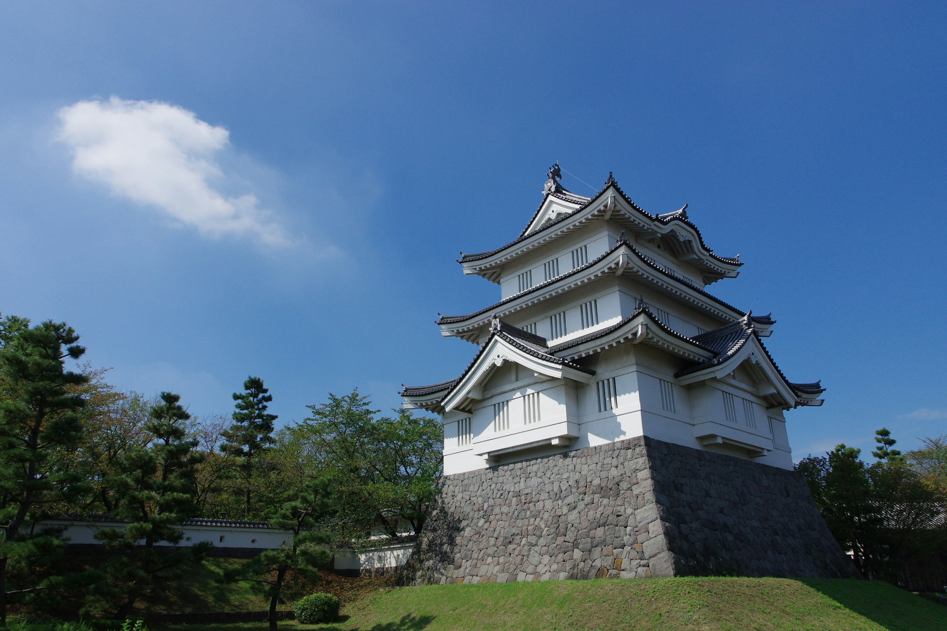 Struktur kastil Jepang yang indah di bawah langit biru dengan pepohonan hijau