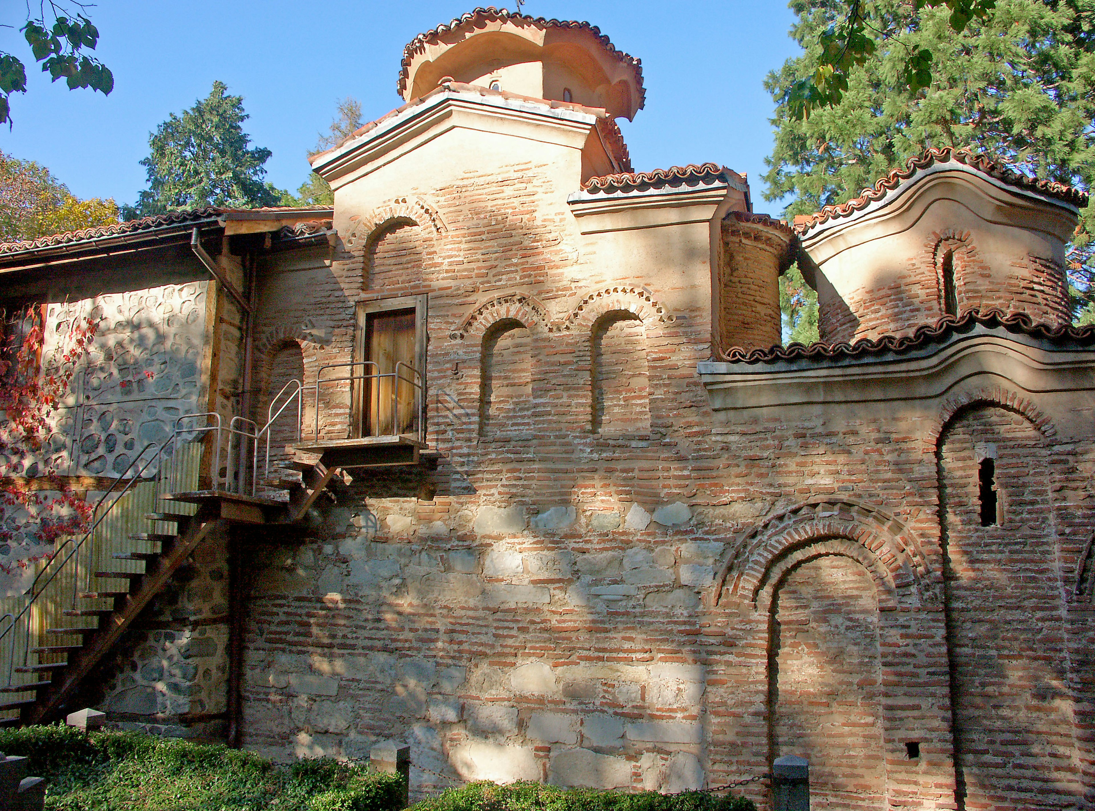 Extérieur d'un bâtiment historique avec un toit rouge et des murs en briques, comprenant des escaliers et une porte en bois