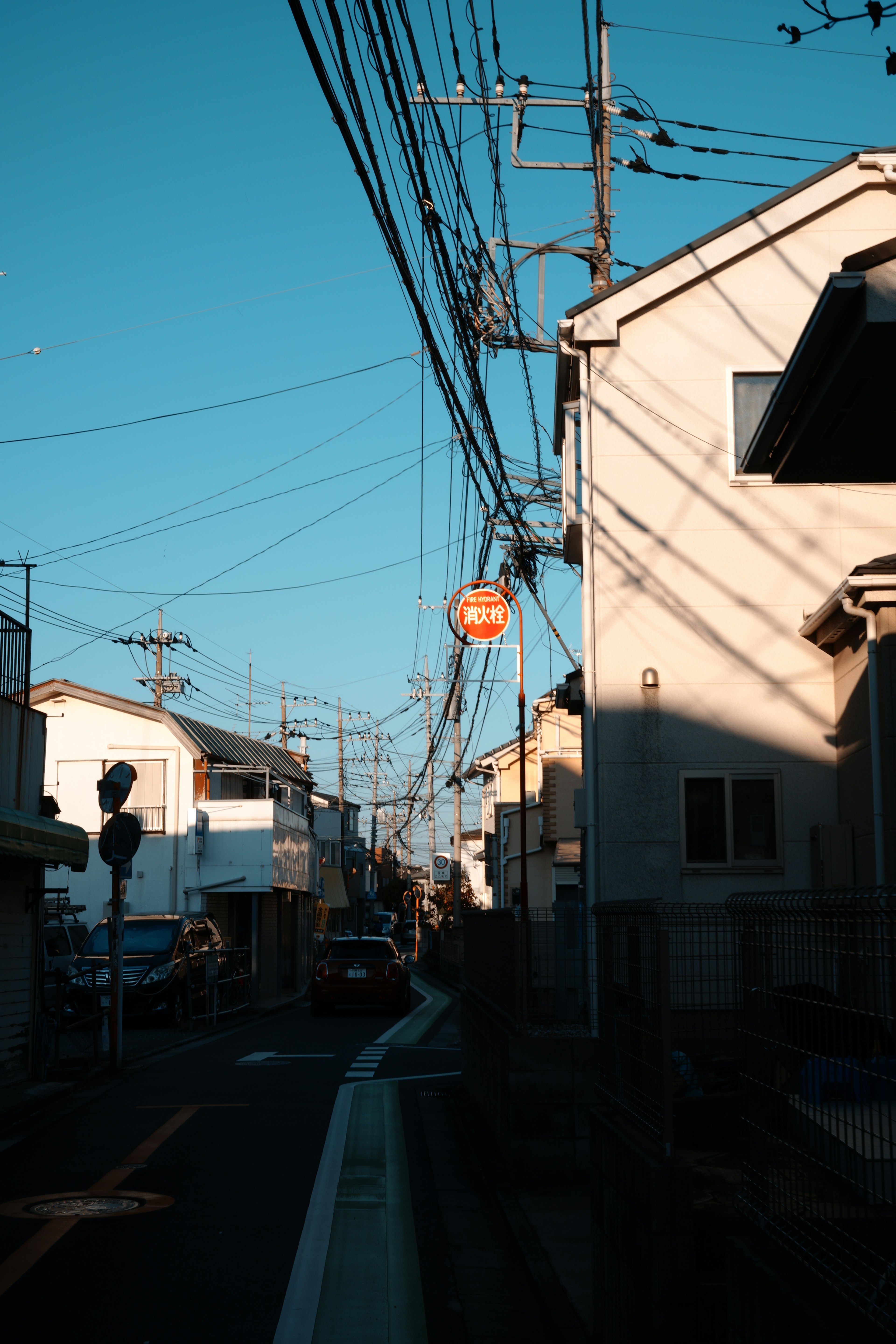 青空の下にある住宅街の通りと電線の影