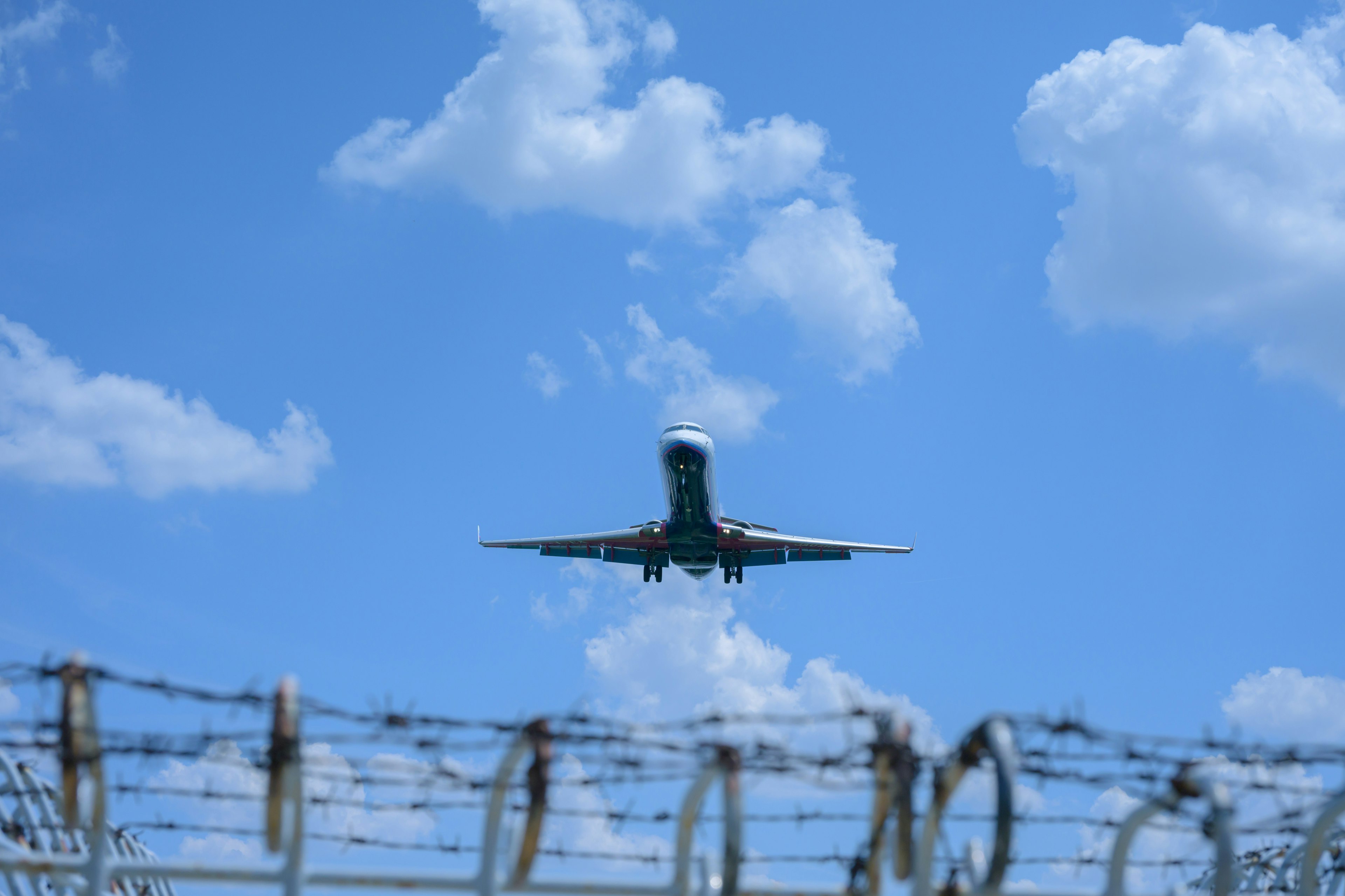 Image d'un avion atterrissant sous un ciel bleu avec des nuages et du fil barbelé