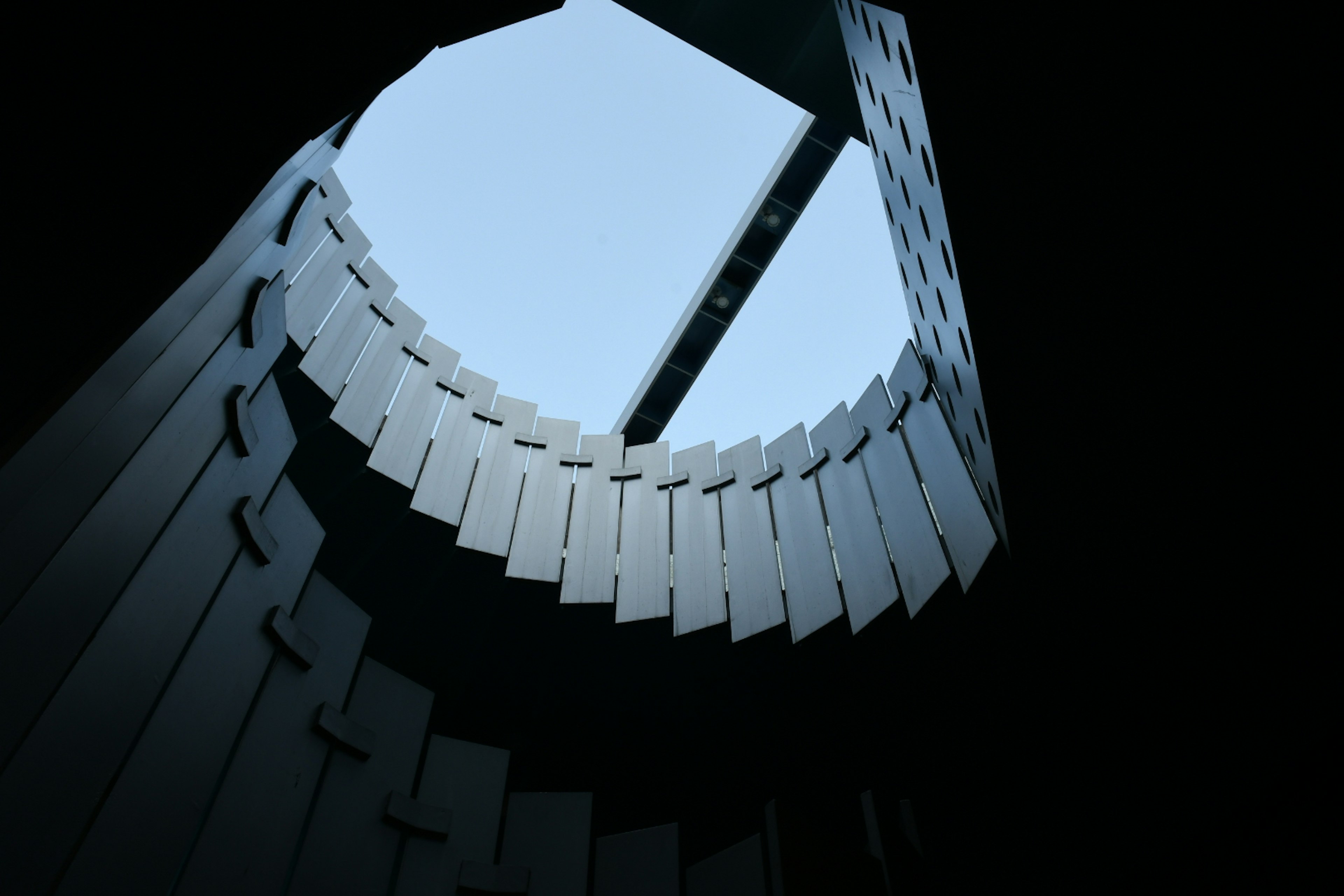 View looking up inside a building showcasing a circular opening with a visible sky and linear structure