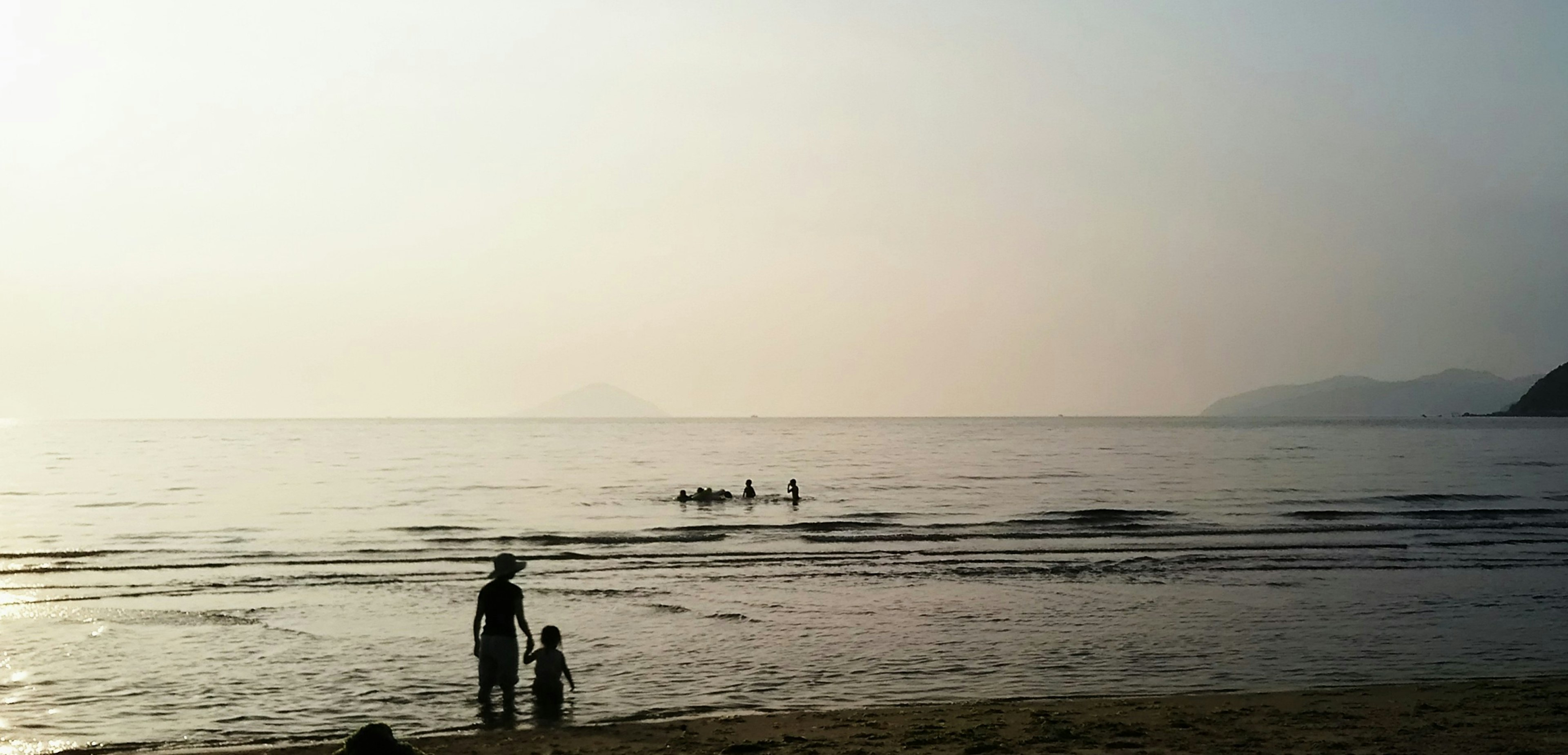 Silhouette einer Familie am Strand mit fernen Figuren im Wasser