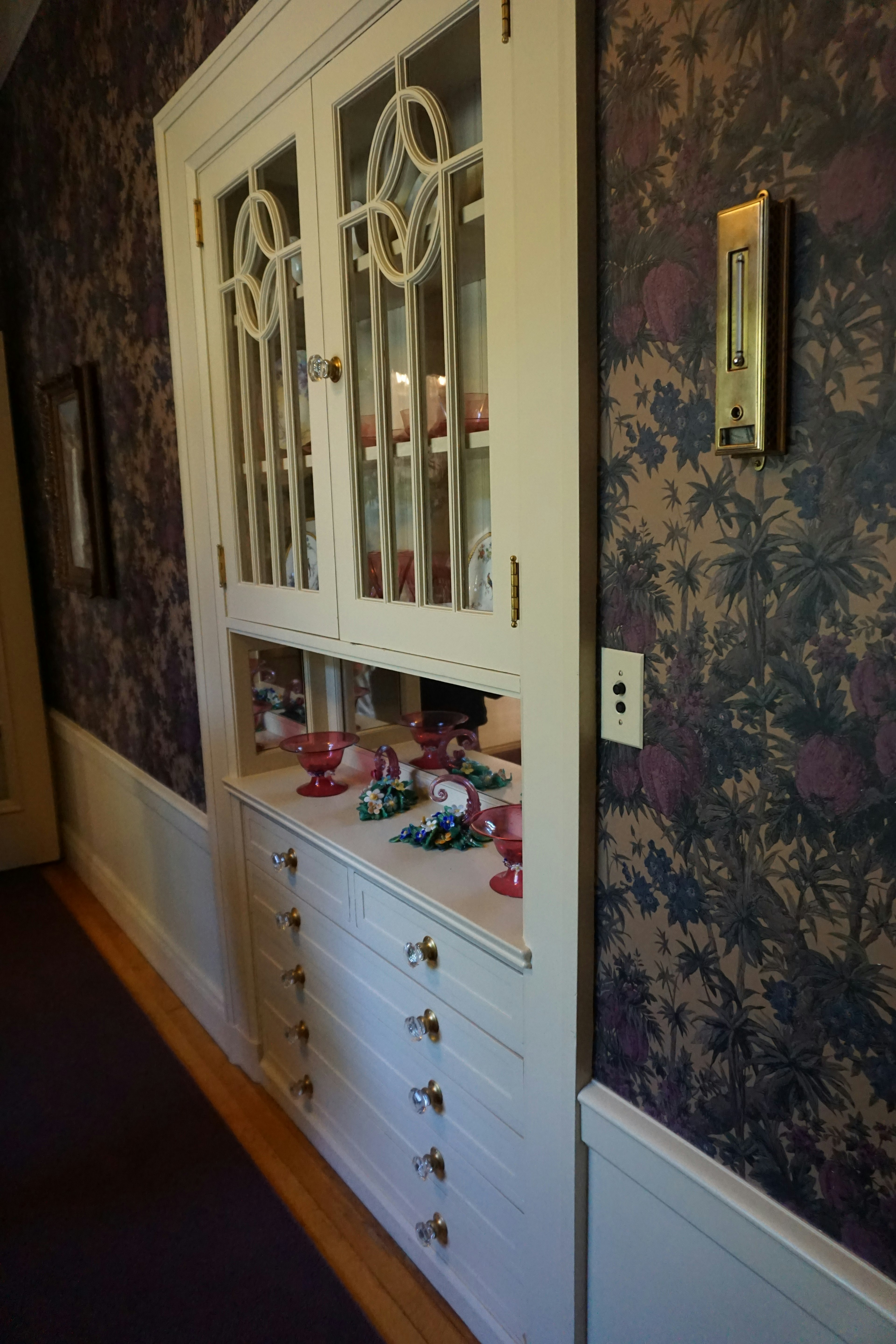 A hallway featuring a white cabinet with glass doors and floral wallpaper