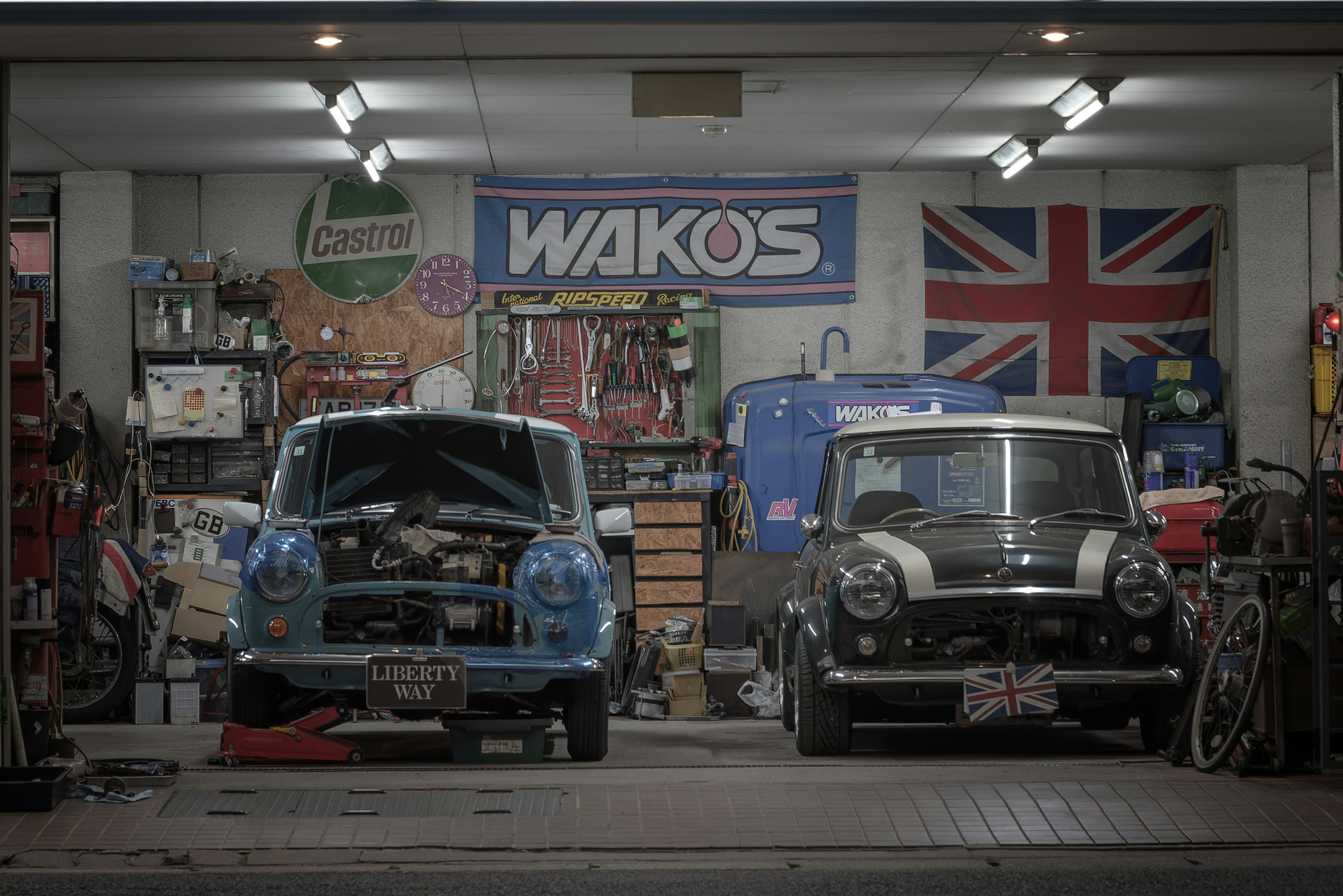 Intérieur d'un garage avec une Mini bleue et une Mini noire outils et une bannière WAKOS visibles