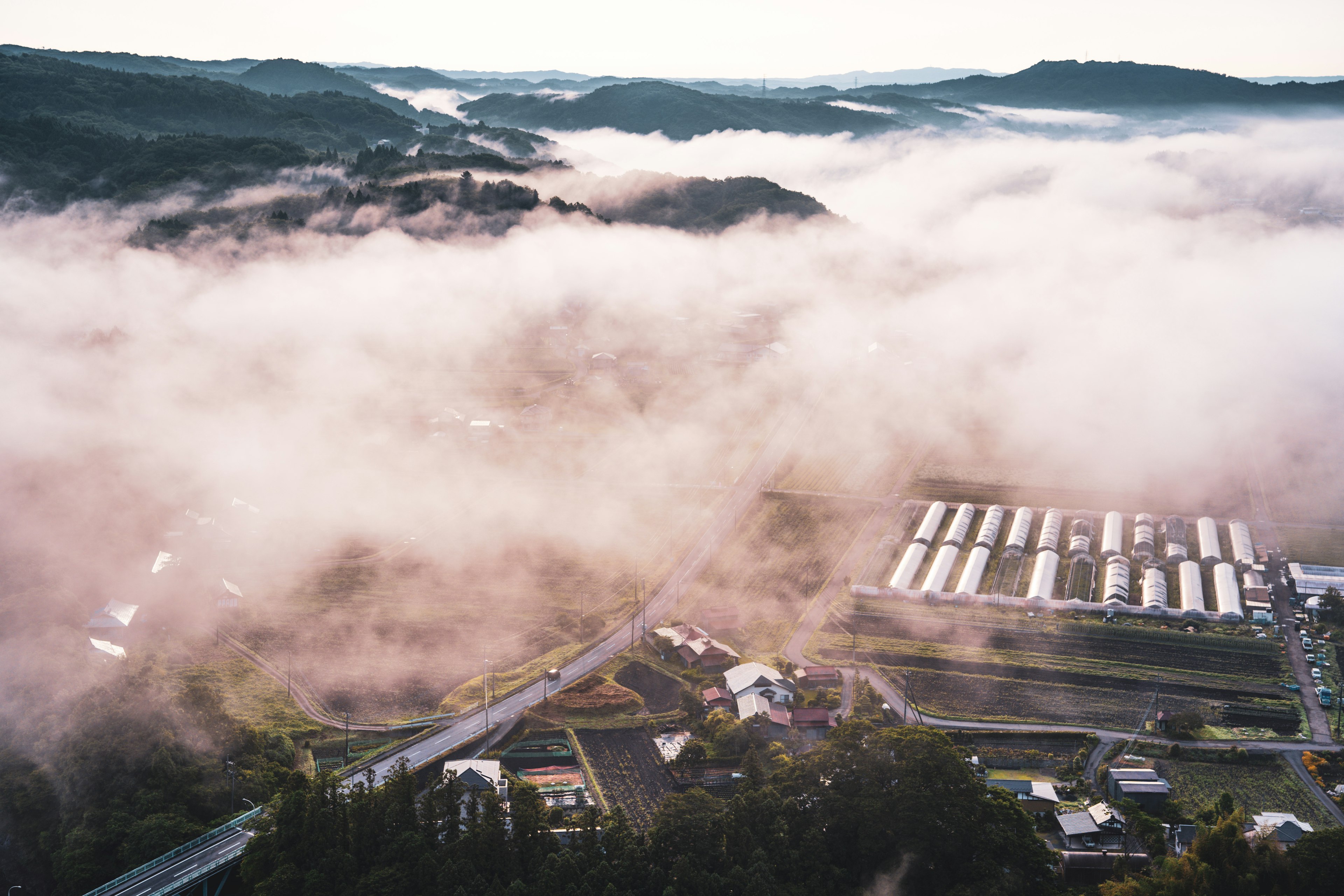 Aerial view of a rural landscape enveloped in fog with mountains in the background