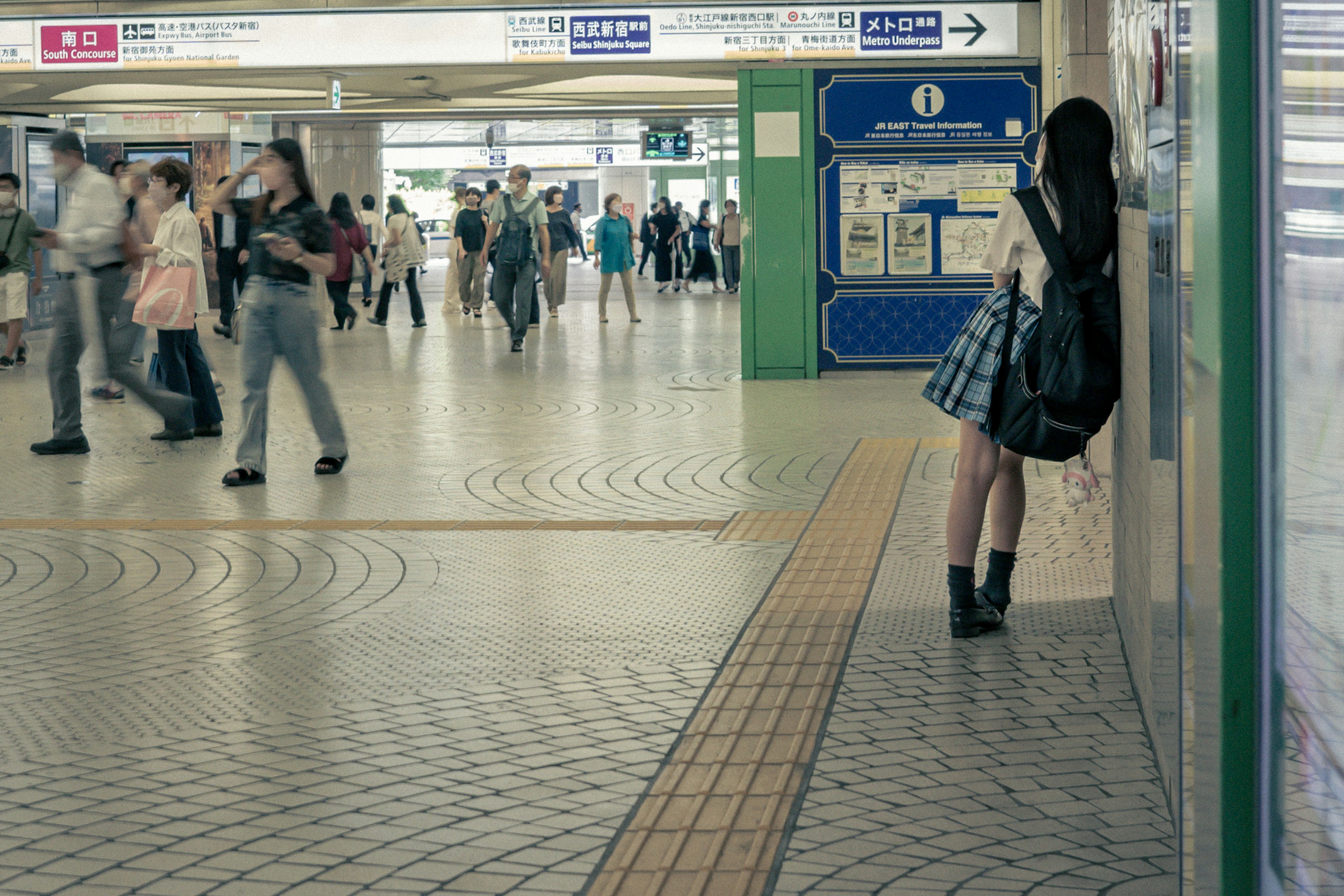 Une fille étudiante attendant dans le hall d'une gare avec de nombreuses personnes autour