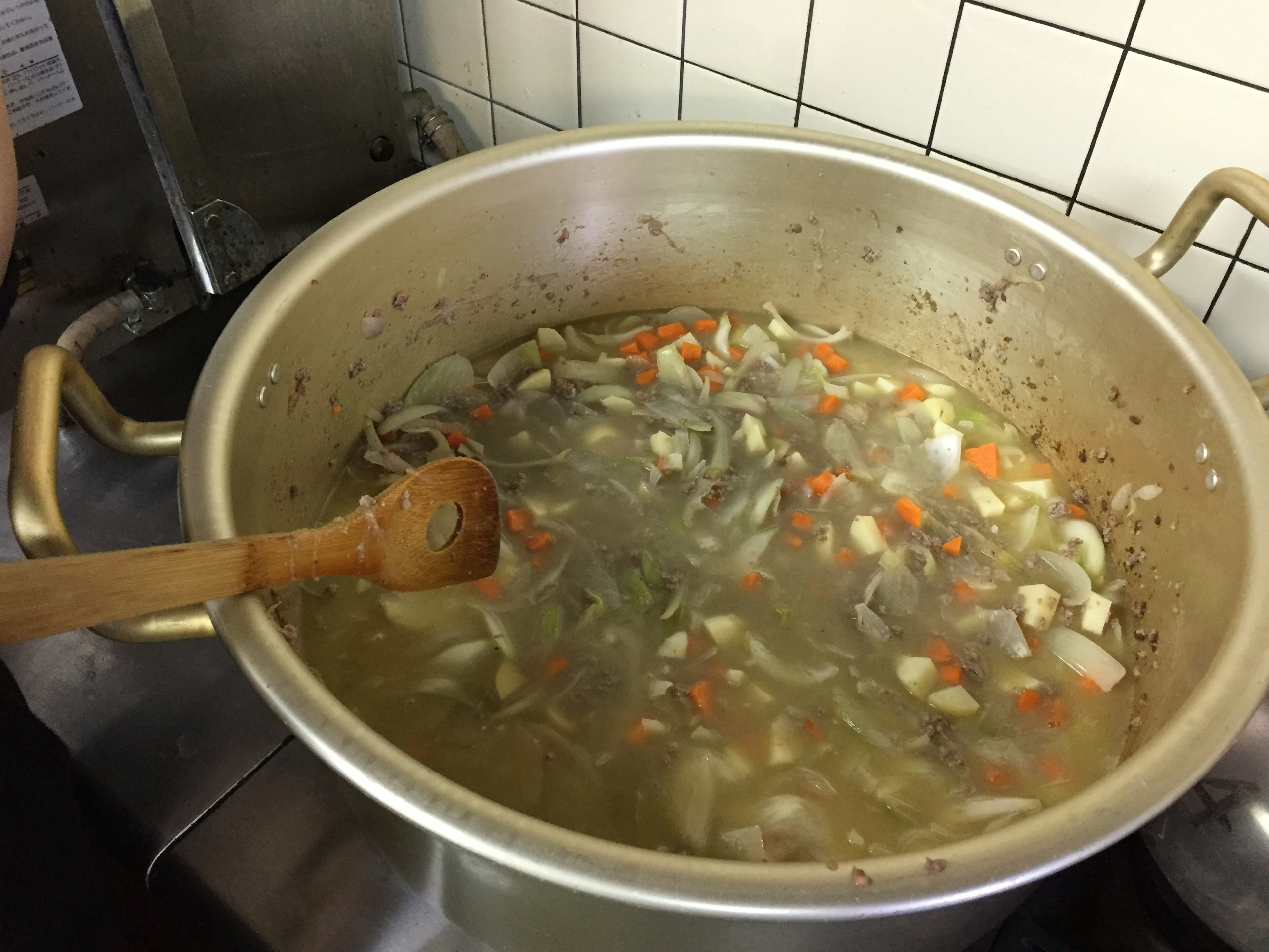 A large pot of vegetable soup being cooked with various chopped vegetables