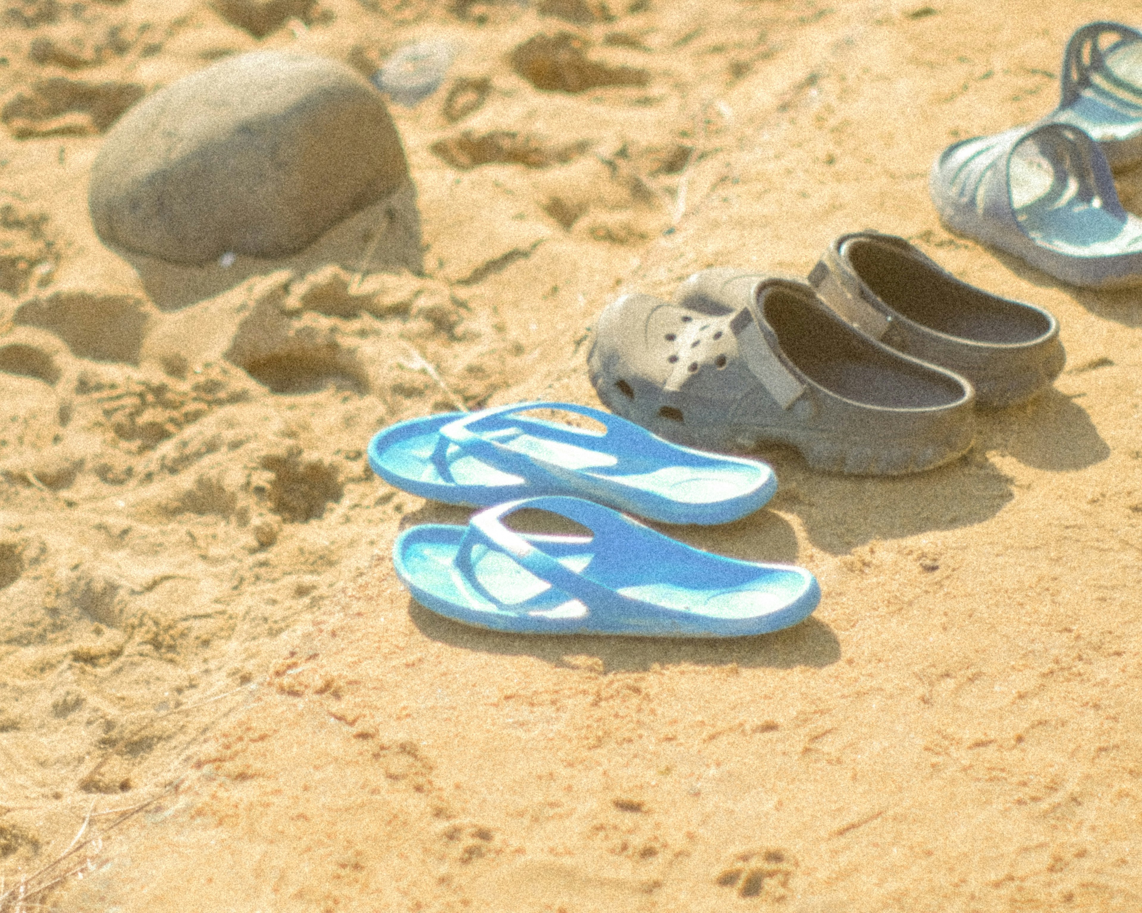 Des tongs bleues et des crocs noirs alignés sur une plage de sable