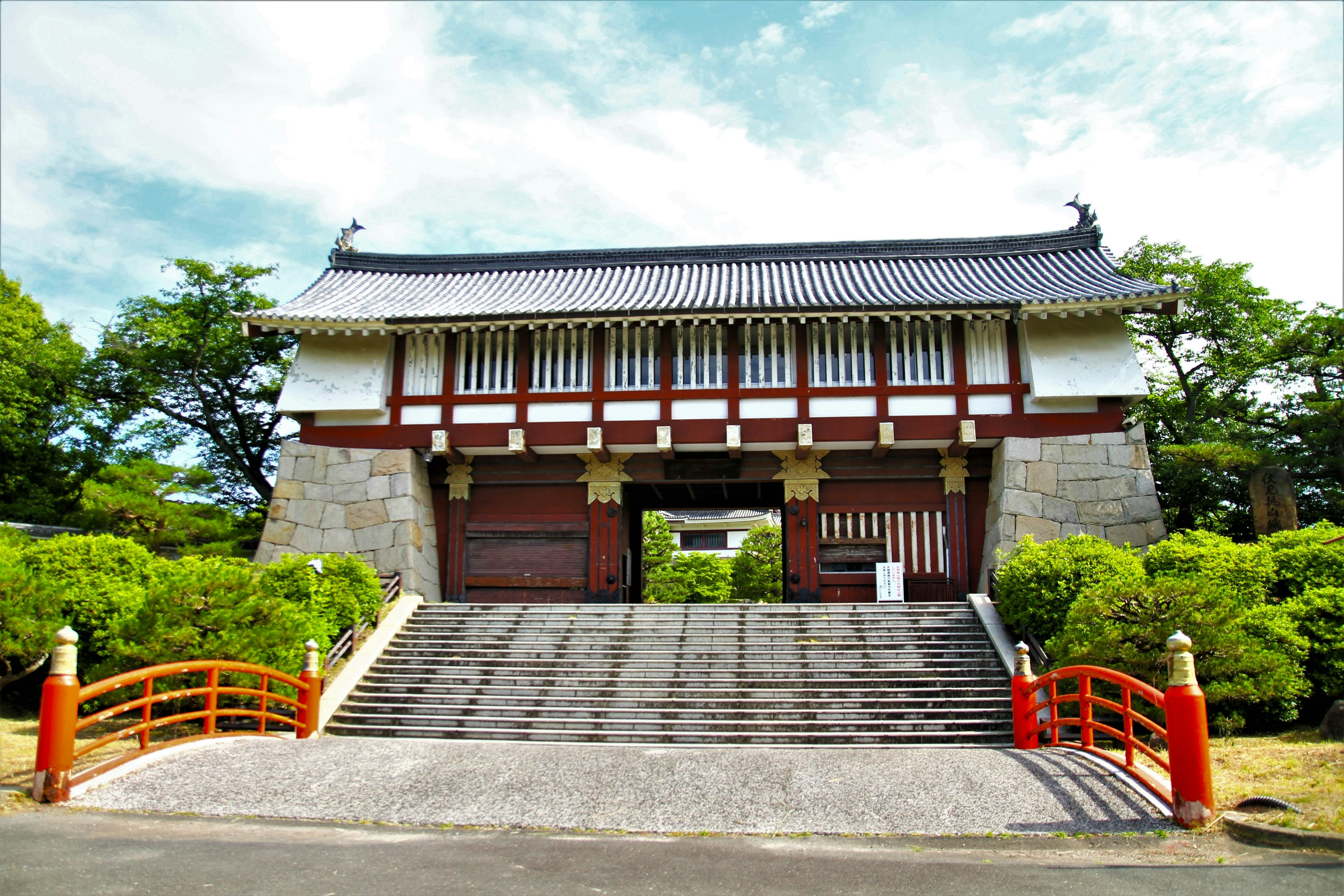 Puerta japonesa tradicional rodeada de vegetación y un puente rojo