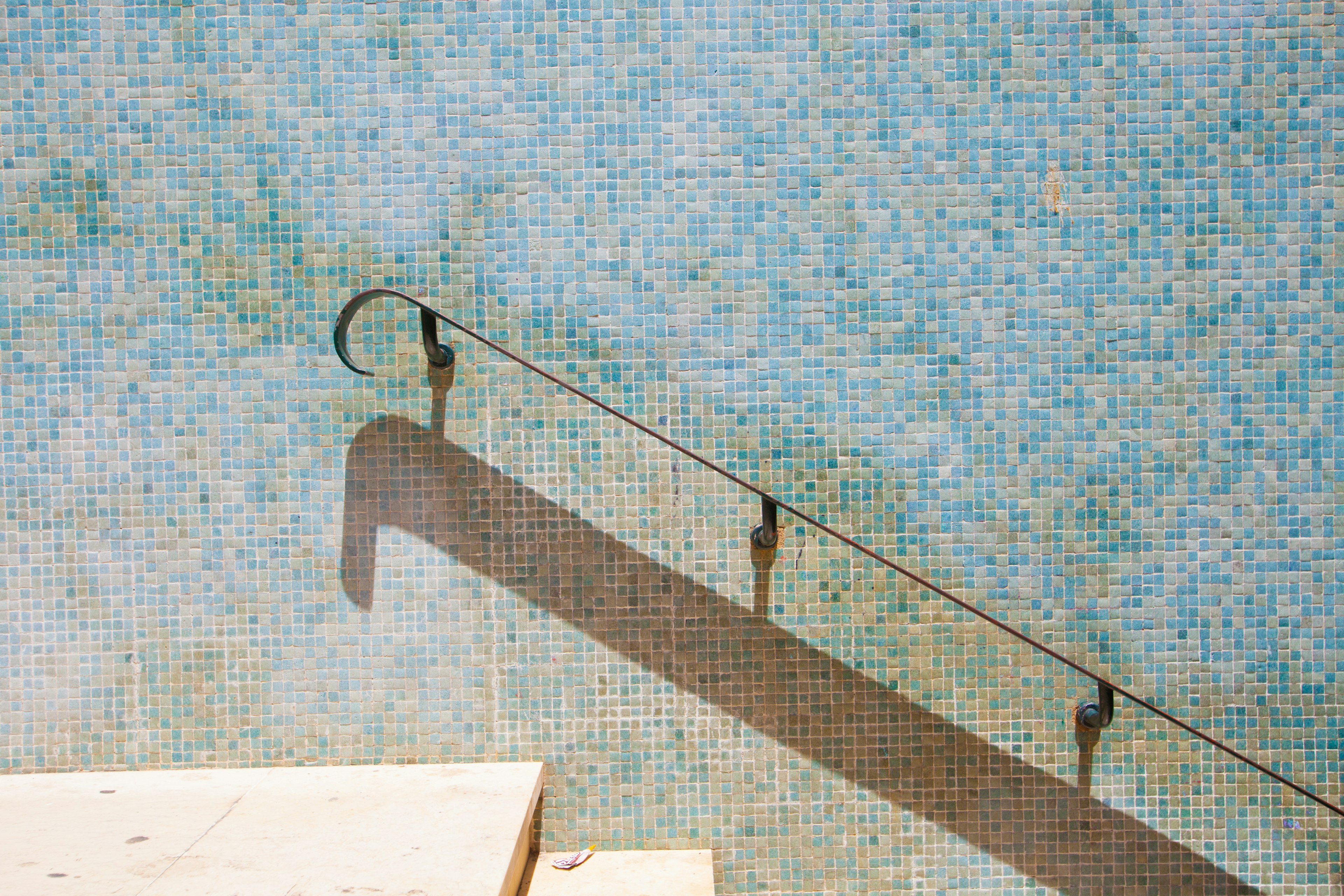 Metal handrail casting a shadow against a blue tiled wall