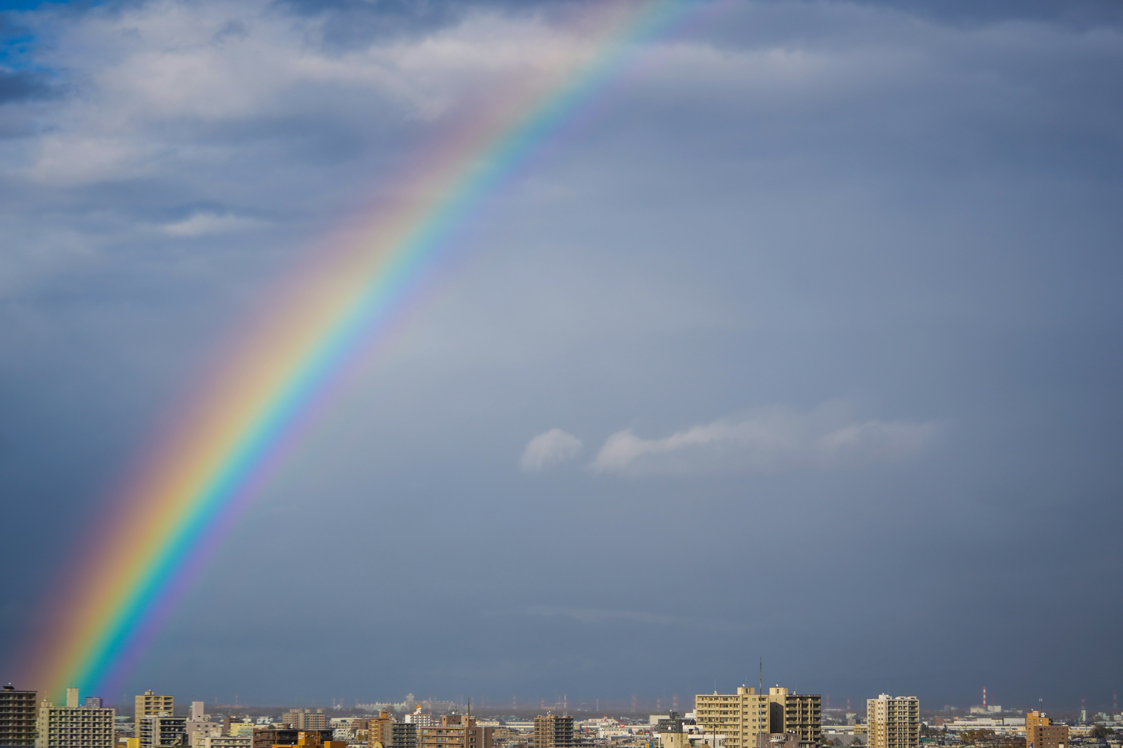 Regenbogen über einer Stadtsilhouette unter einem blauen Himmel