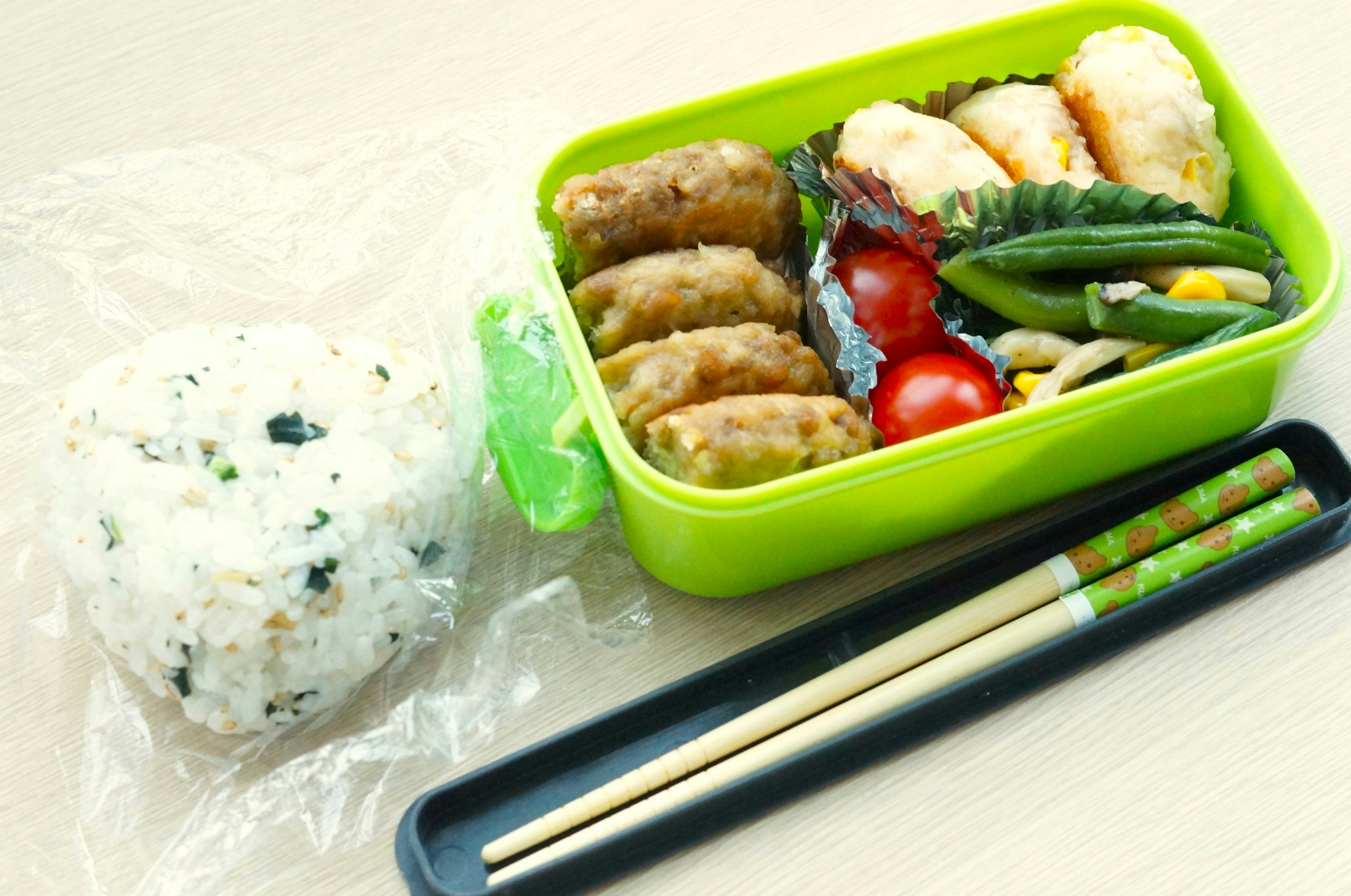 A green bento box filled with various side dishes and a small rice ball