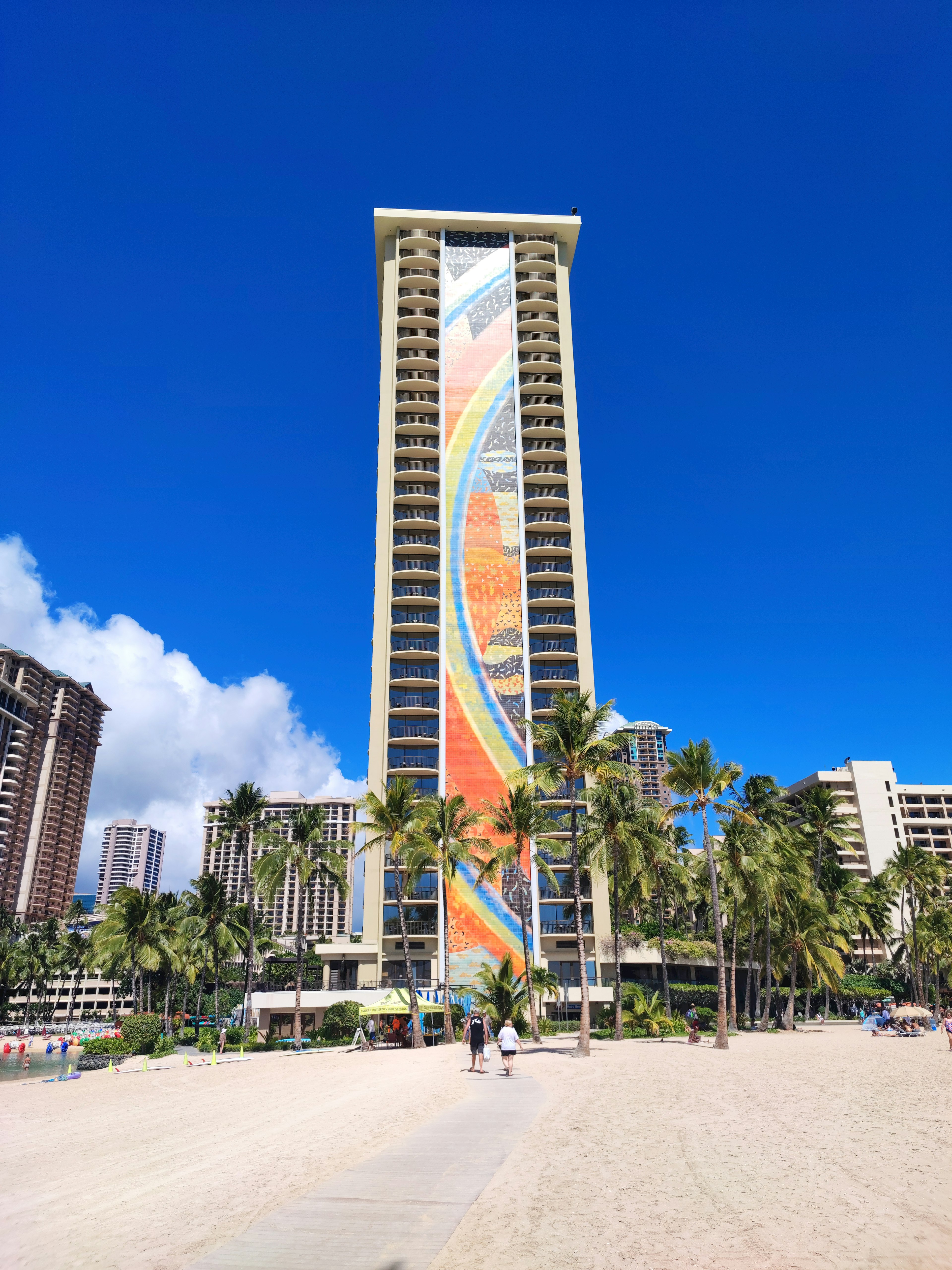 Colorful mural on a beachfront high-rise building under a clear blue sky