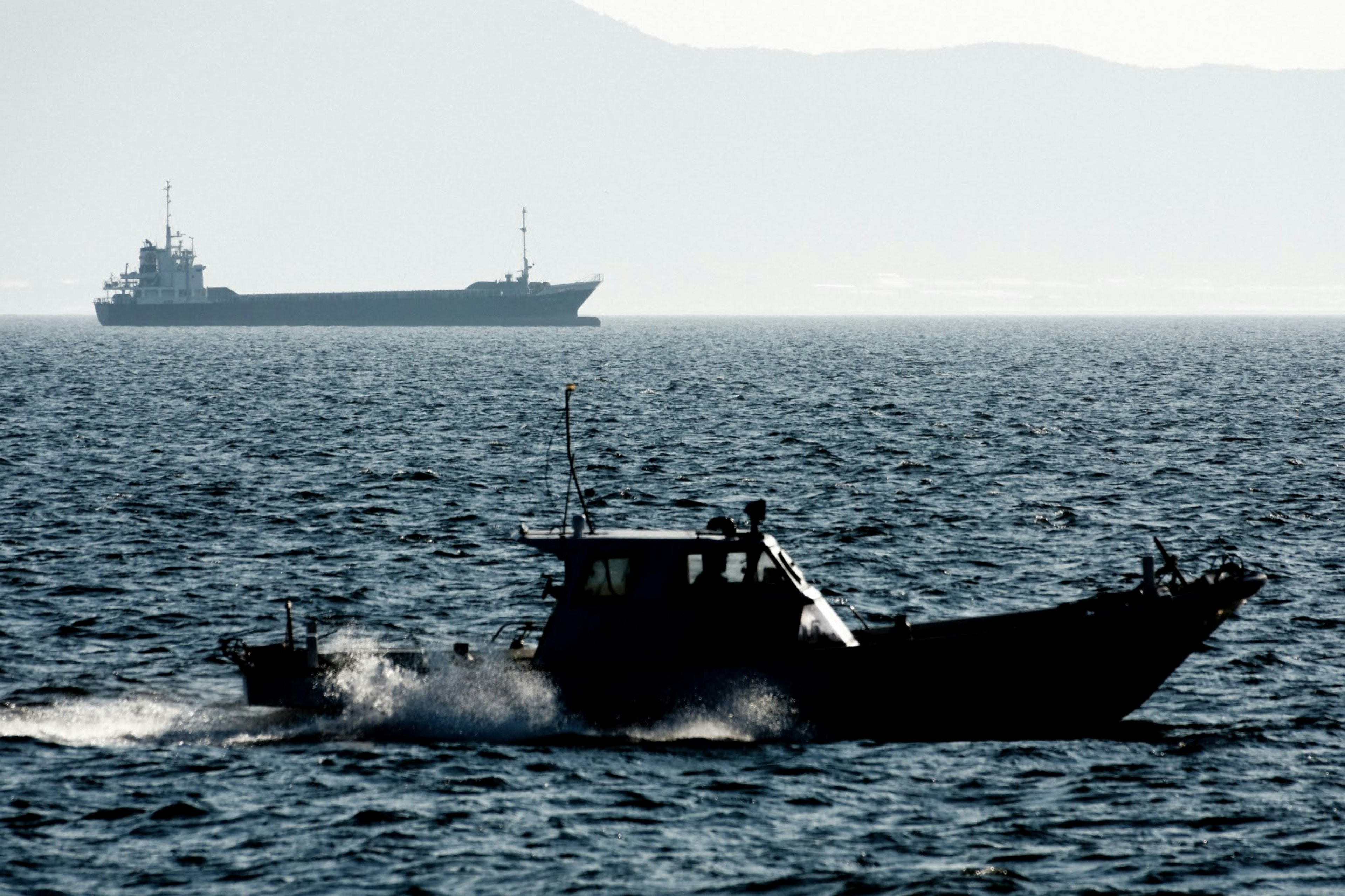 Una piccola barca che si muove sul mare con una grande nave cargo sullo sfondo