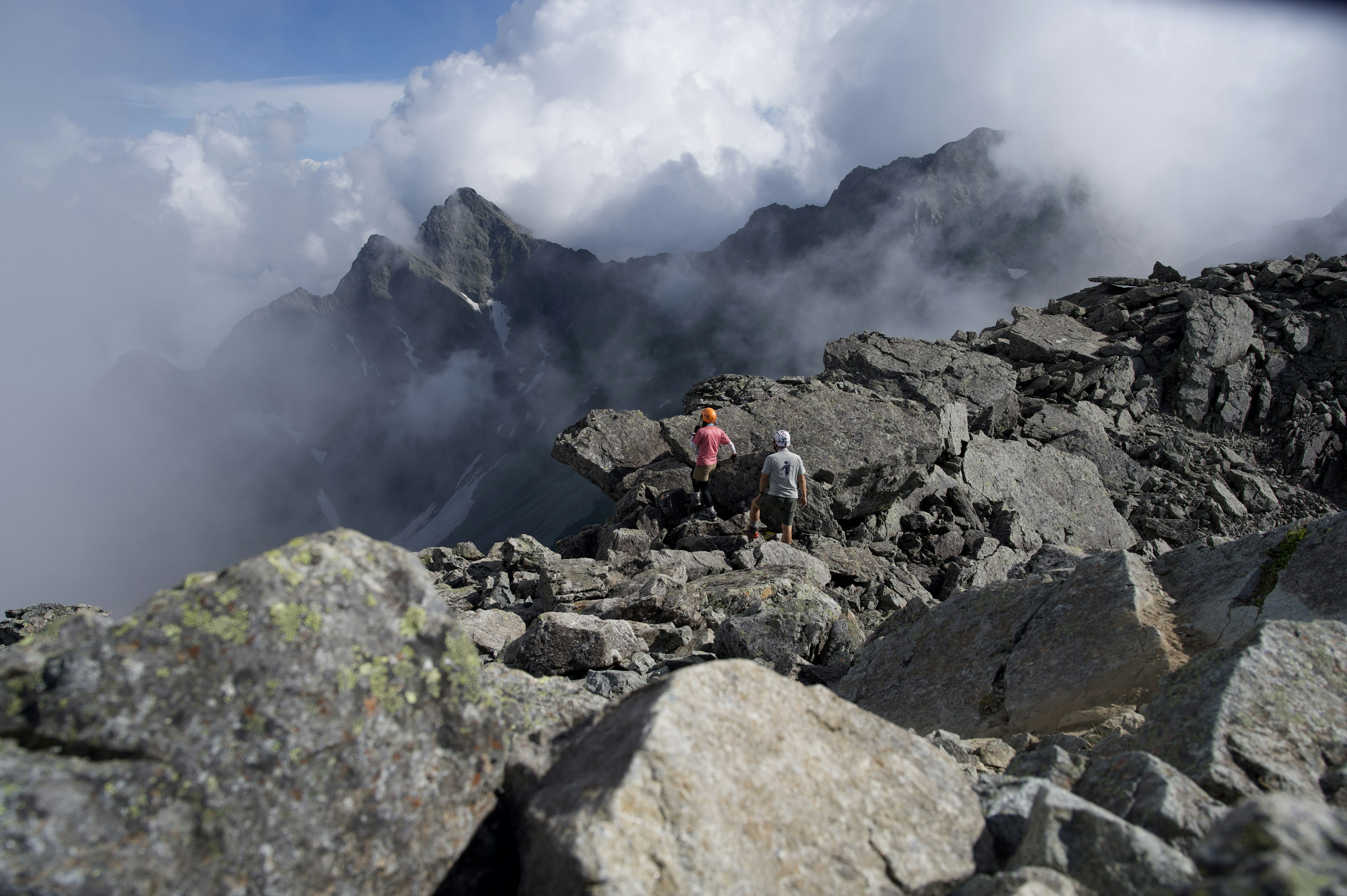 険しい山岳地帯を歩く二人の登山者と雲に覆われた風景