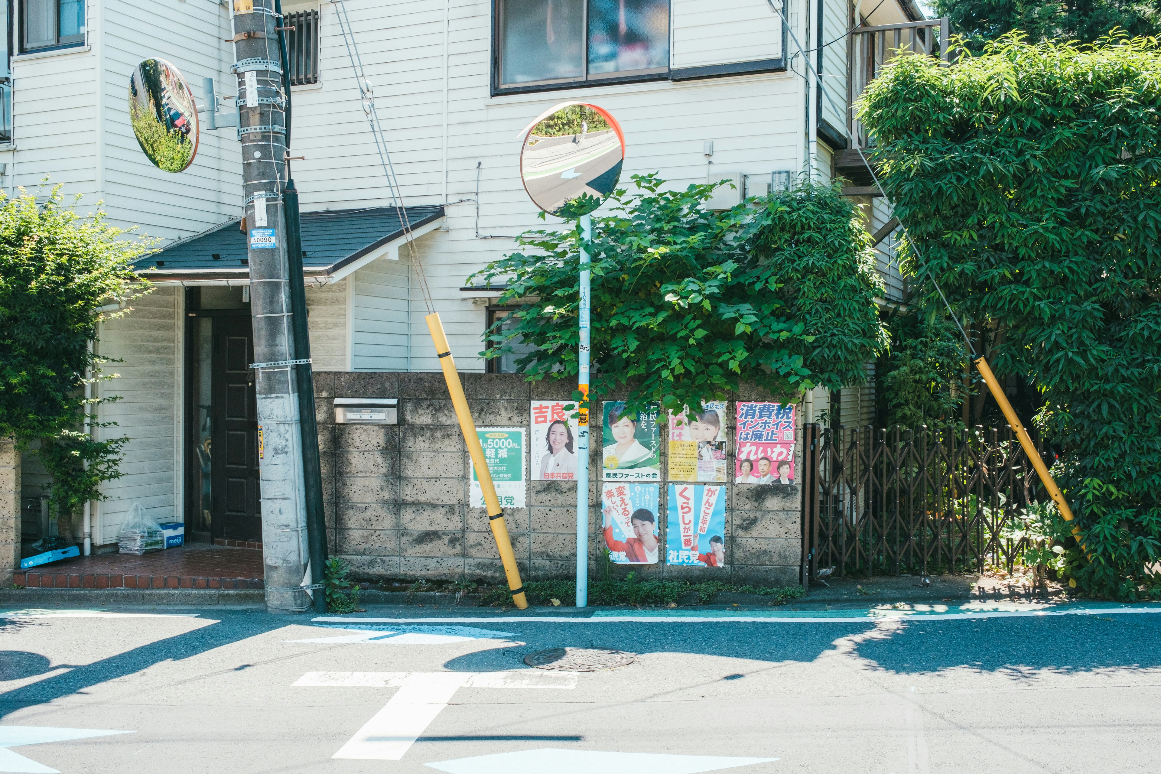 青いバス停とポスターが貼られた壁がある住宅街の風景