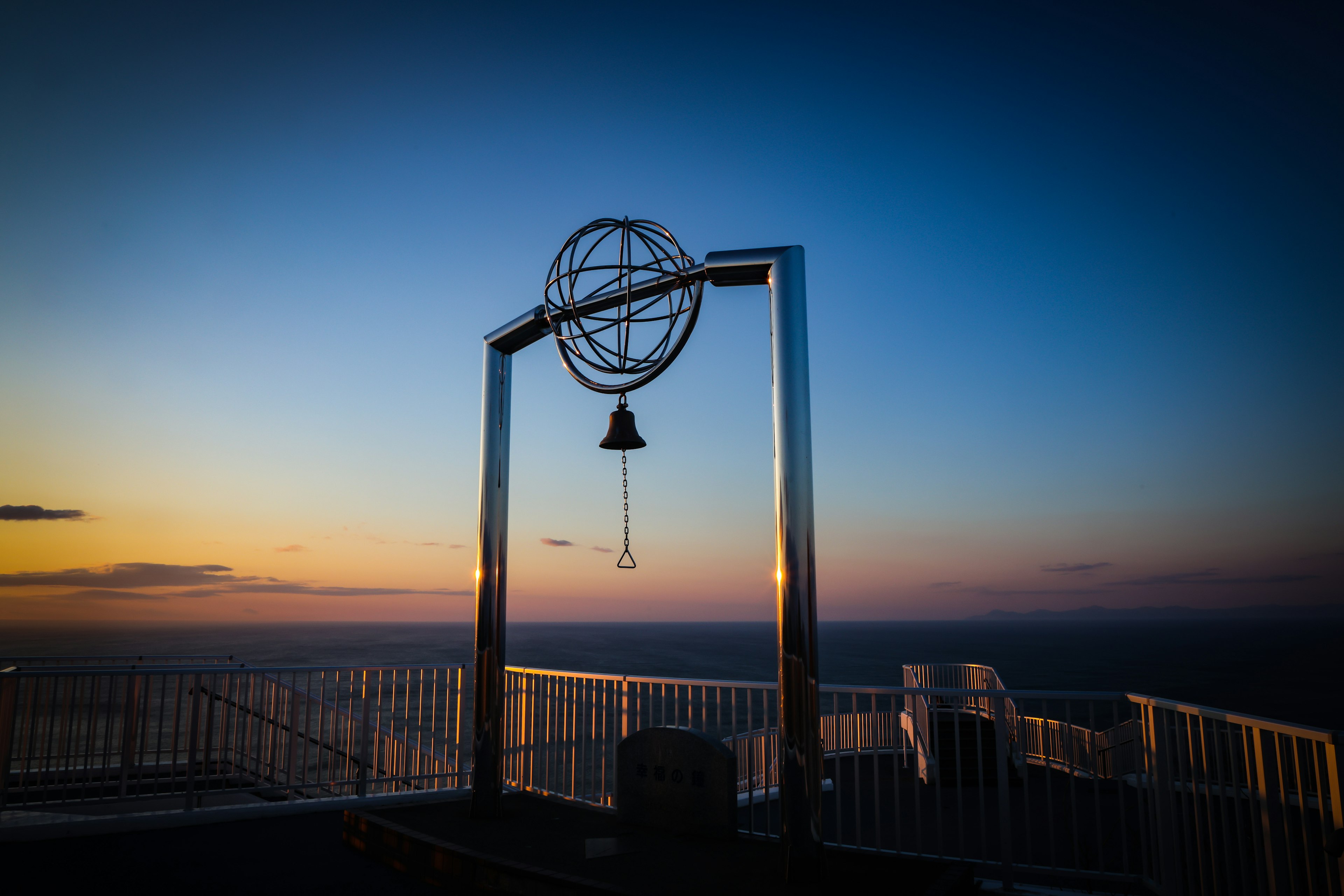 Campana y escultura de globo contra un fondo de océano al atardecer