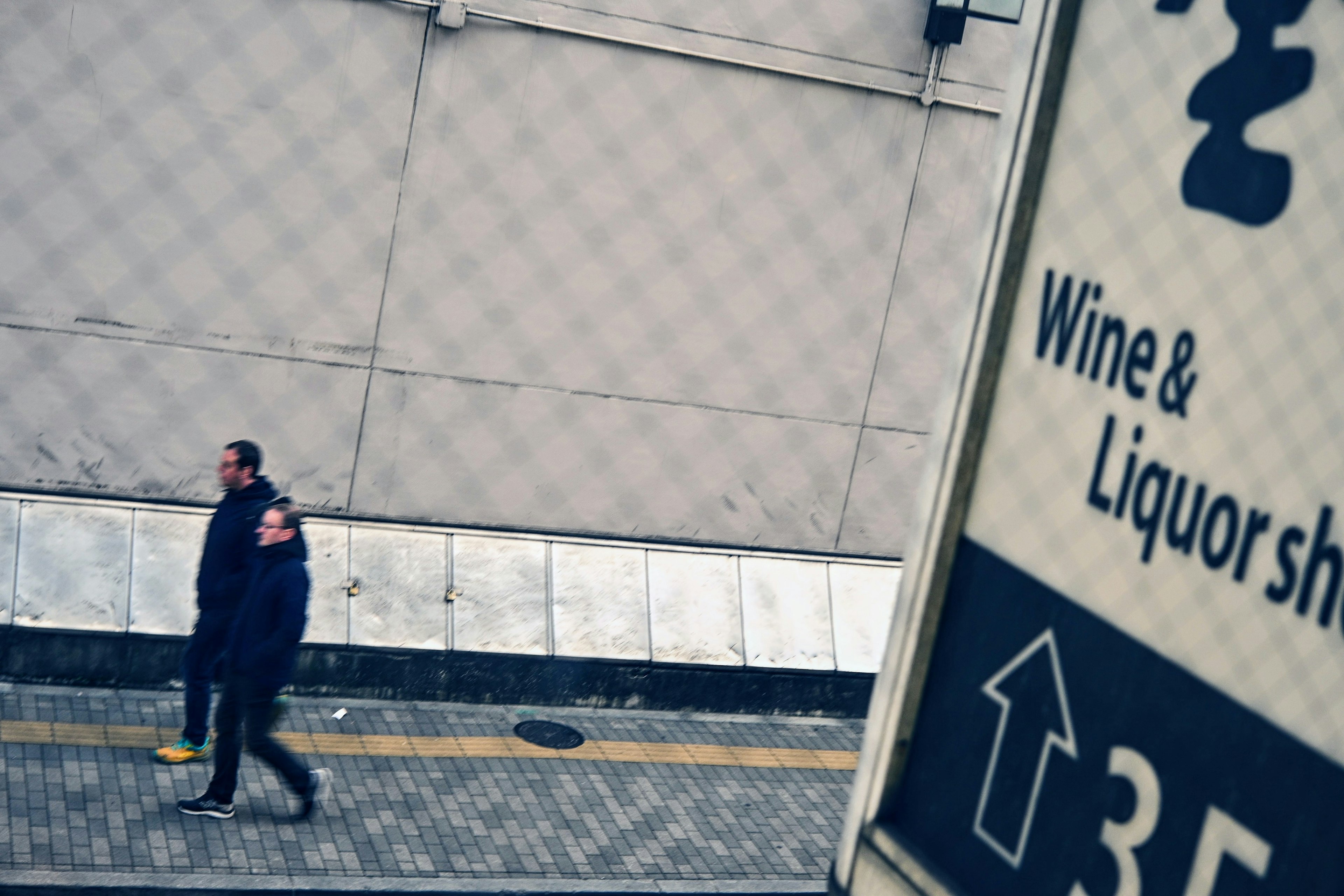 Two men walking in front of a wine and liquor shop sign