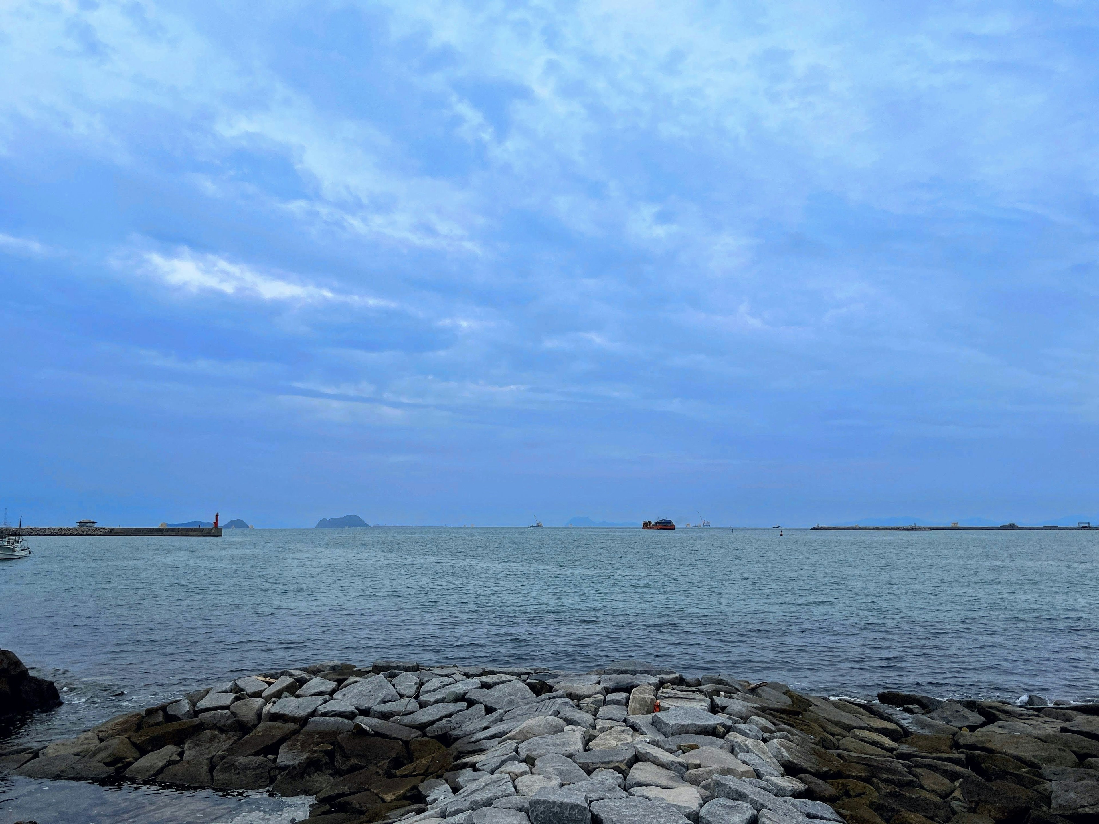 Paesaggio di mare calmo e cielo nuvoloso con molo di rocce che si estende nell'acqua