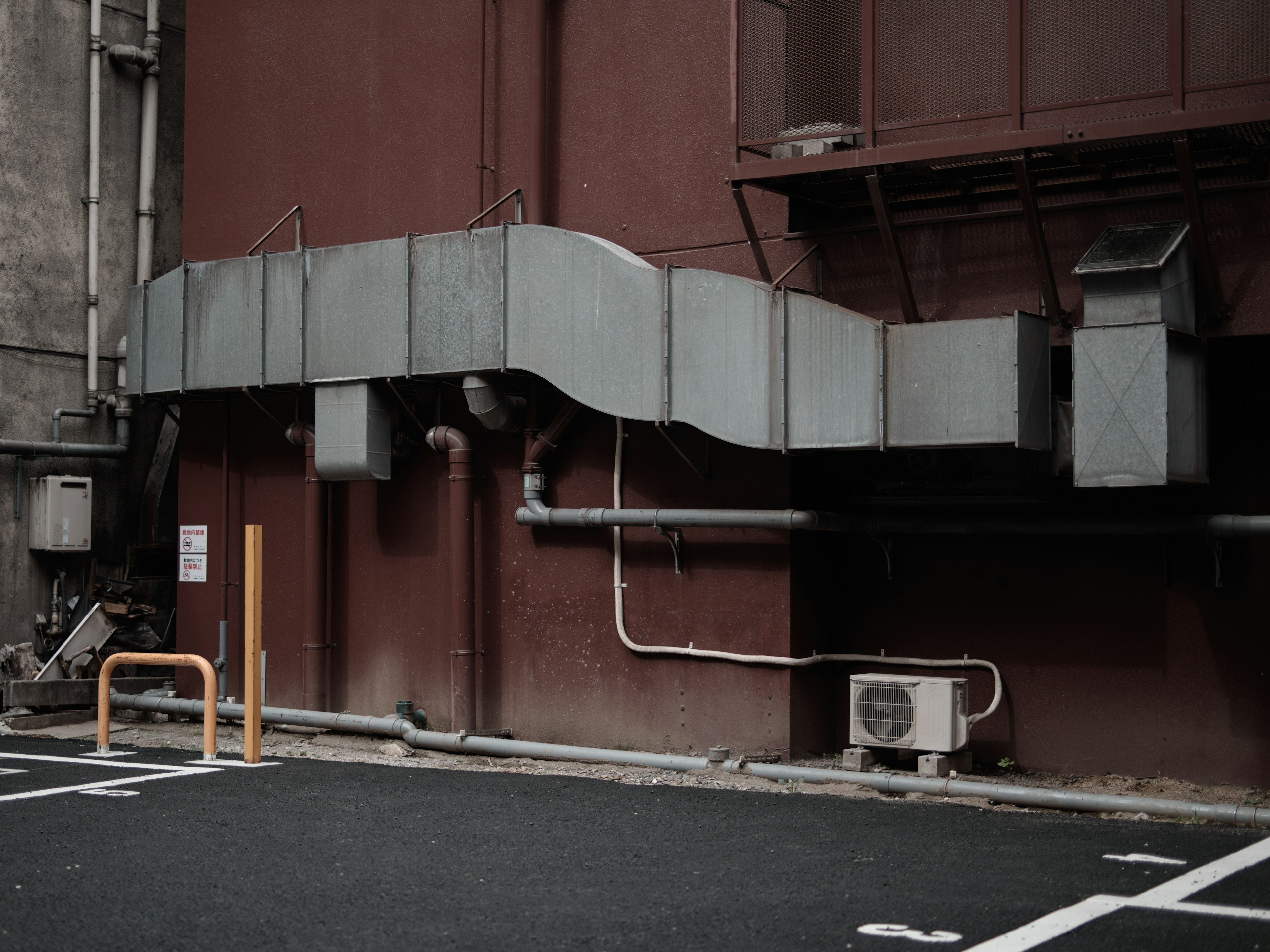 Ducts métalliques et tuyaux fixés au mur rouge d'un bâtiment