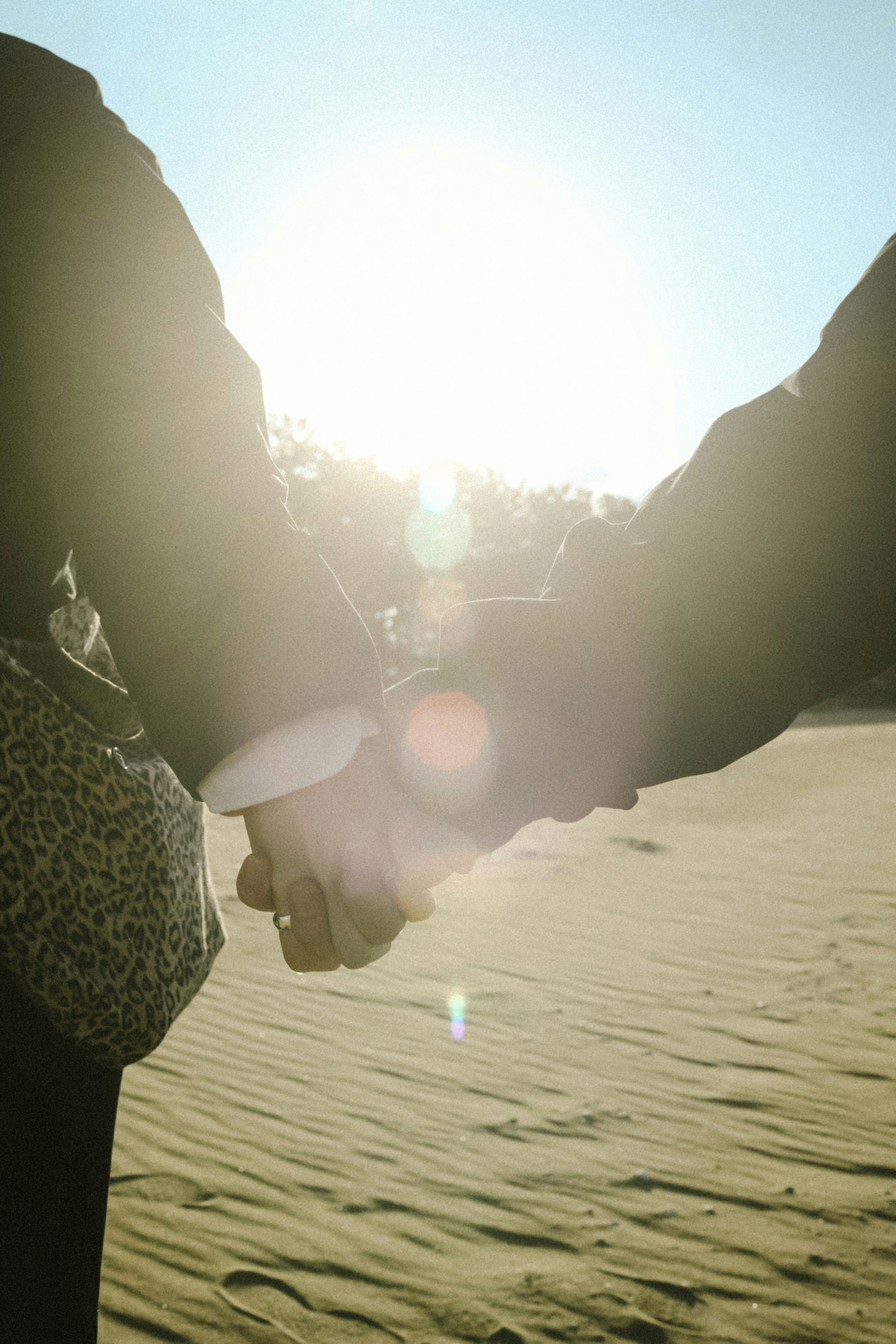 Silhouette of a couple holding hands in sunlight on a sandy beach