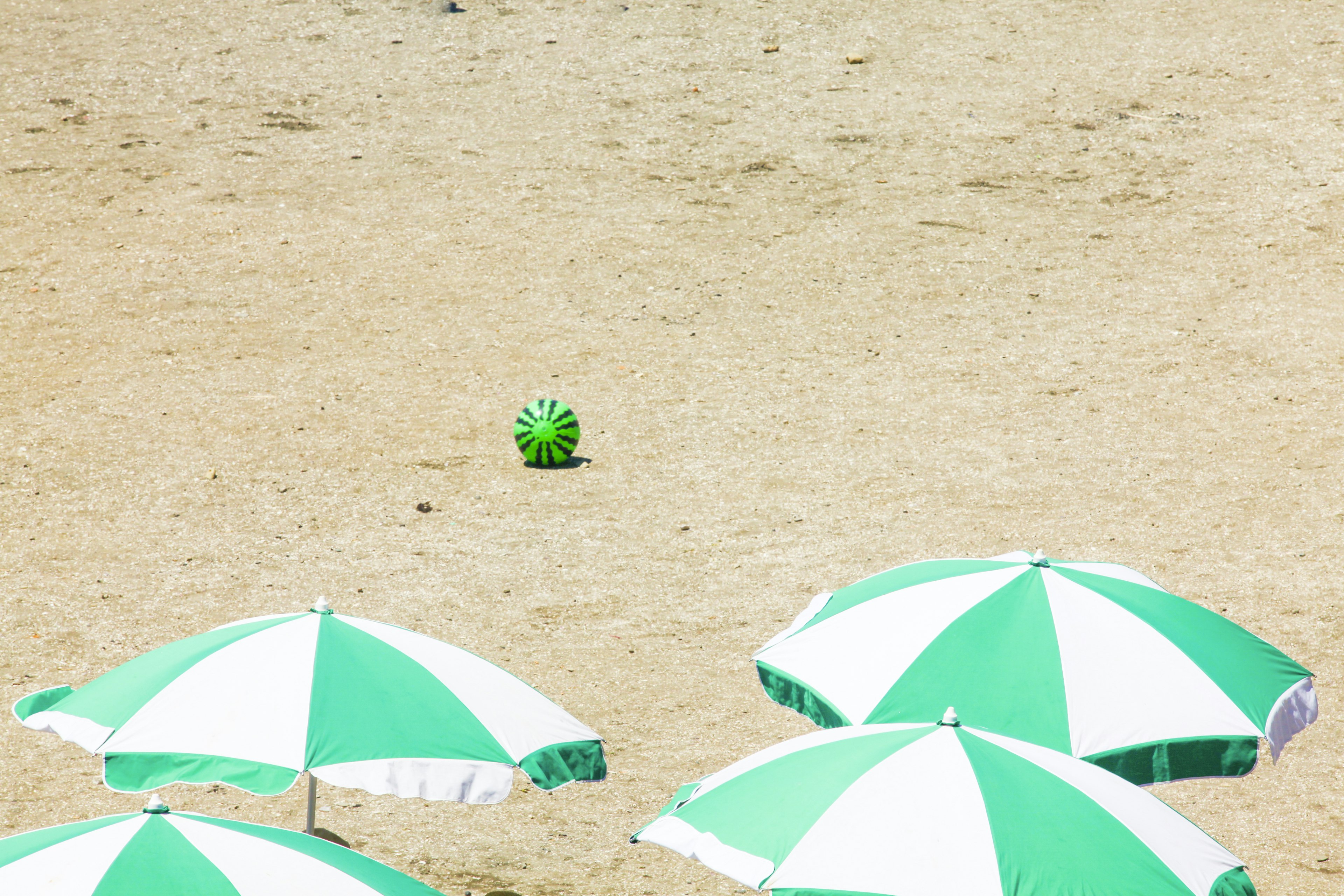 Pelota colorida entre sombrillas verdes y blancas en la arena