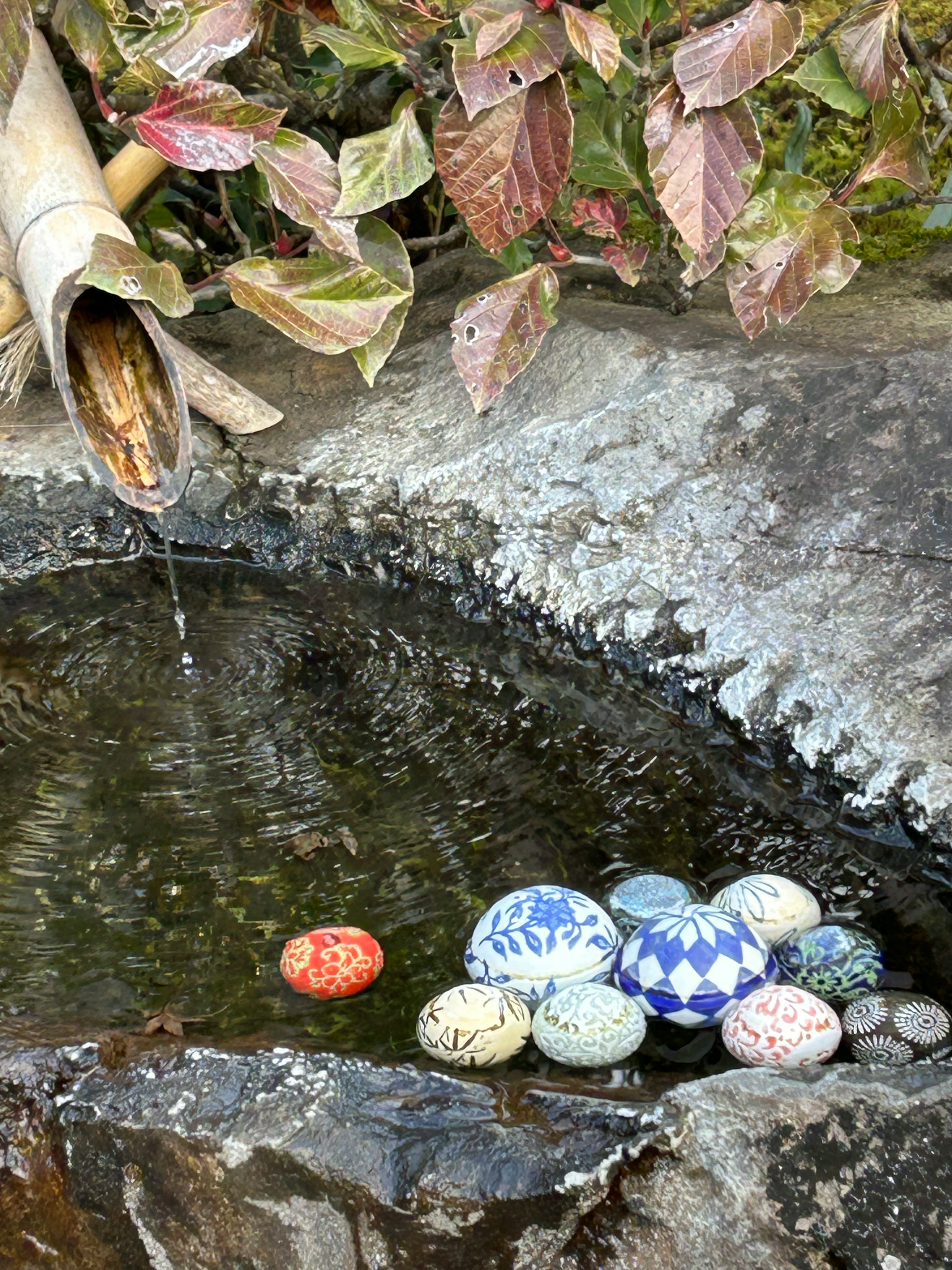 Piedras decorativas coloridas flotando en la superficie tranquila de un estanque con flujo de agua de bambú