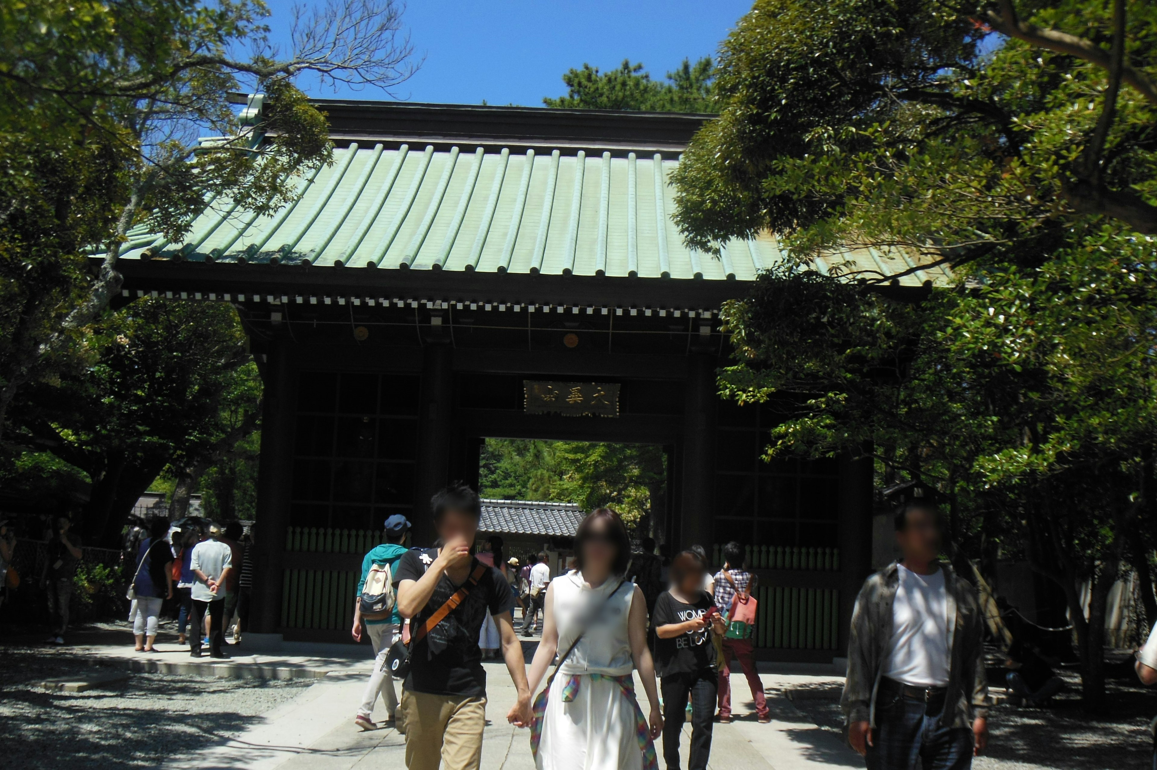 People walking in front of a green-roofed gate surrounded by trees