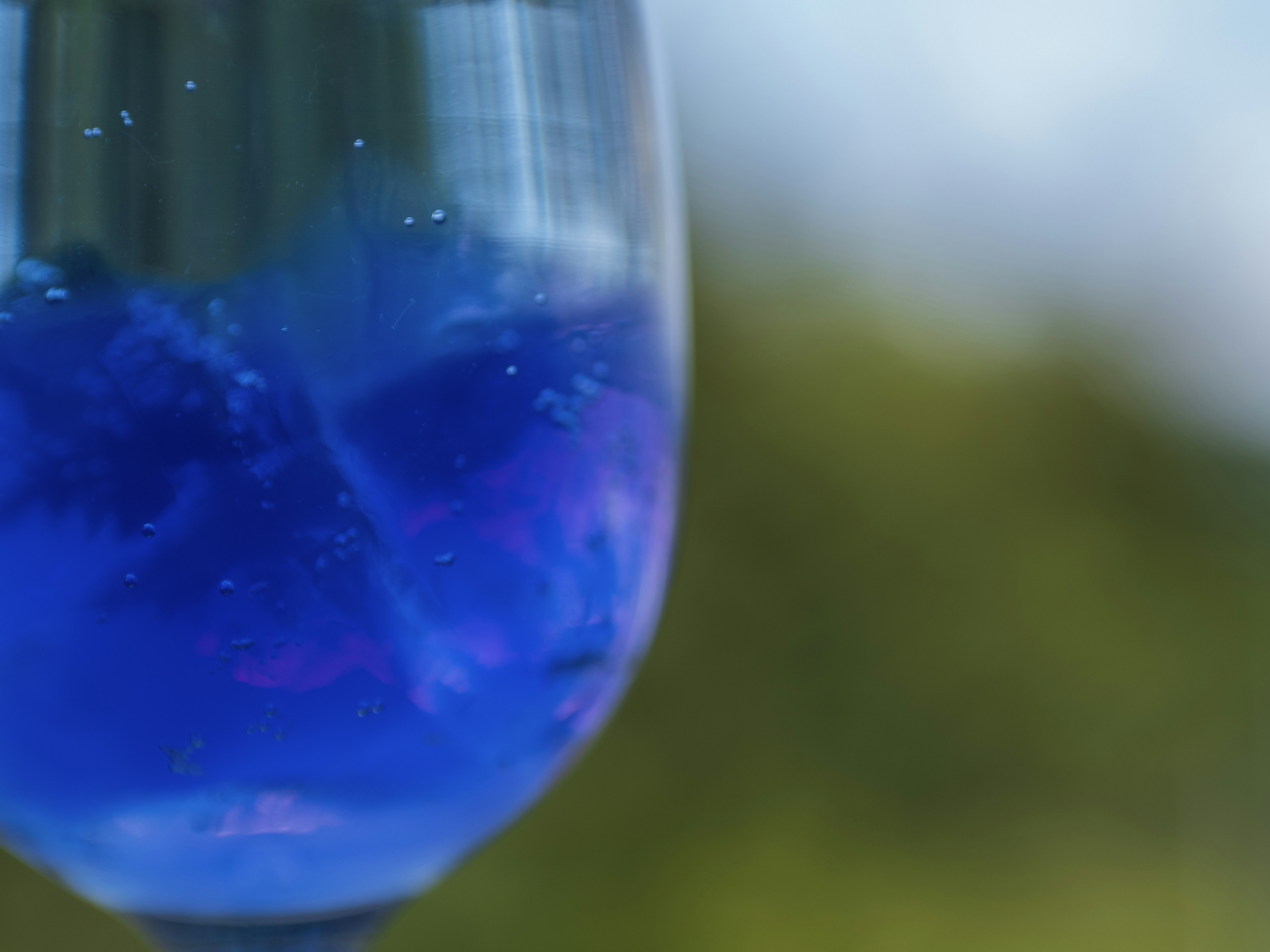 Close-up gelas dengan minuman biru latar belakang hijau kabur