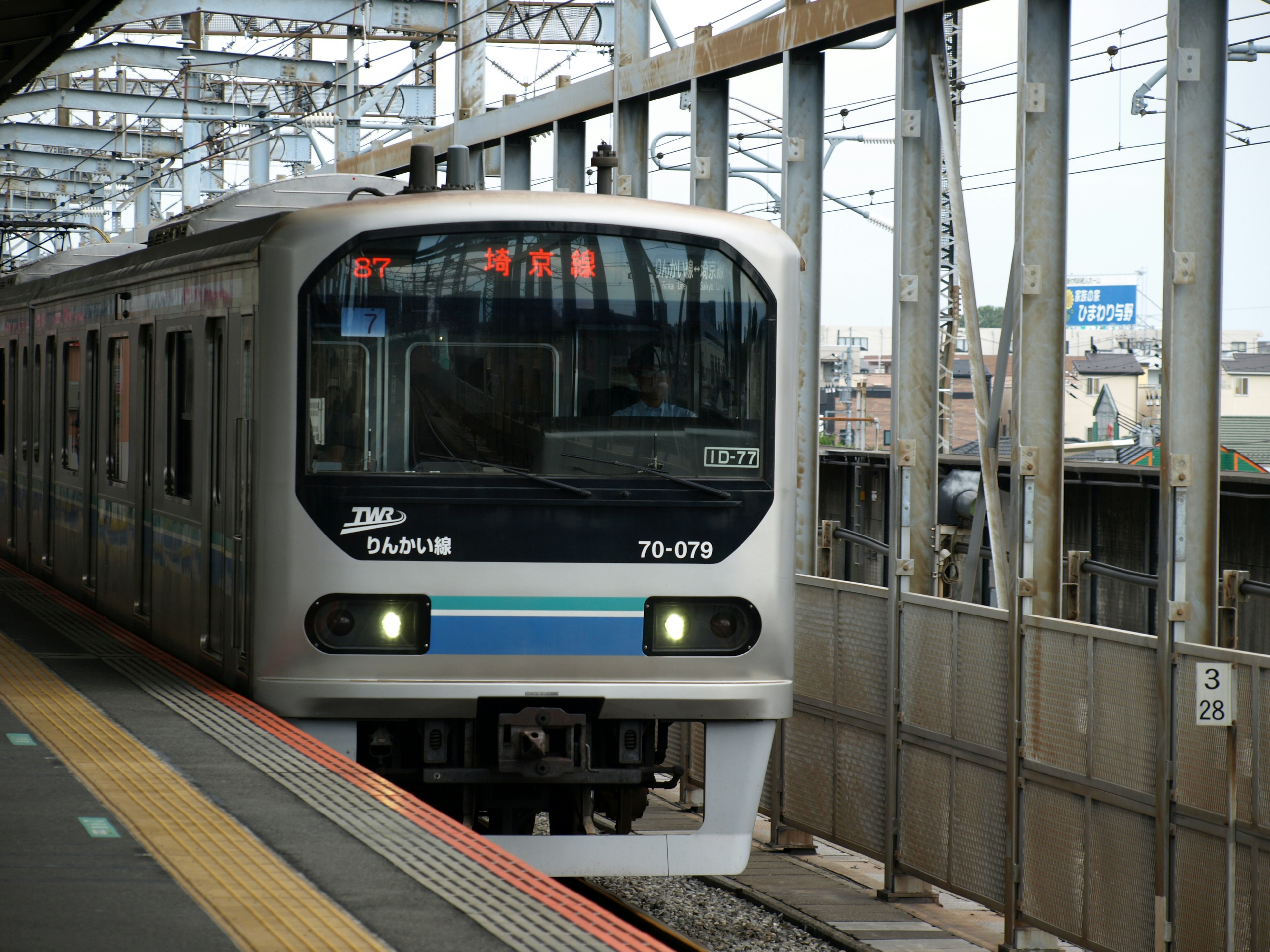 Train argenté s'arrêtant à une gare avec une bande bleue distinctive et des structures ferroviaires environnantes