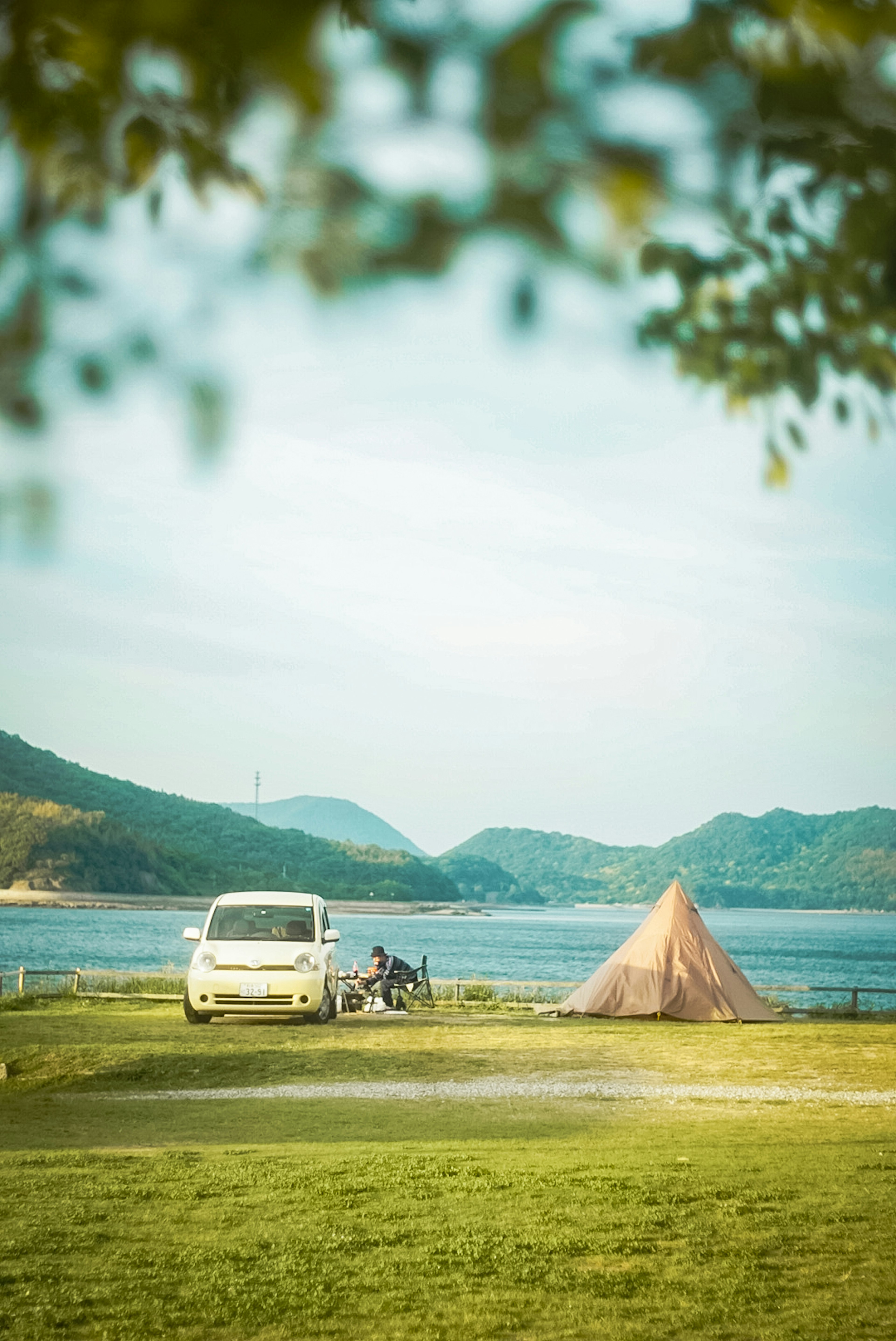 A white vehicle parked near a lake with a tent in the background