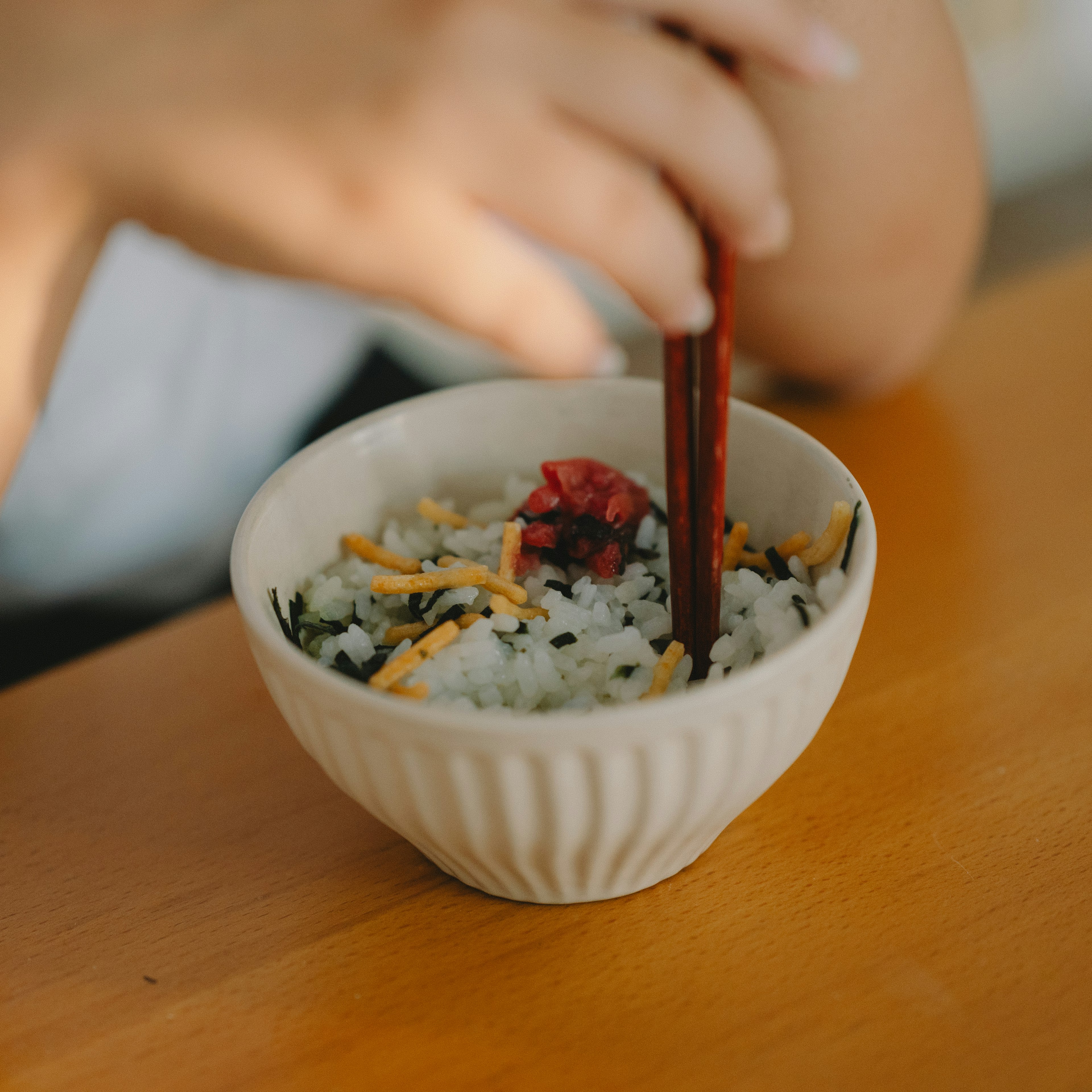 一只手握着筷子在一个装有色彩丰富配料的米饭碗上