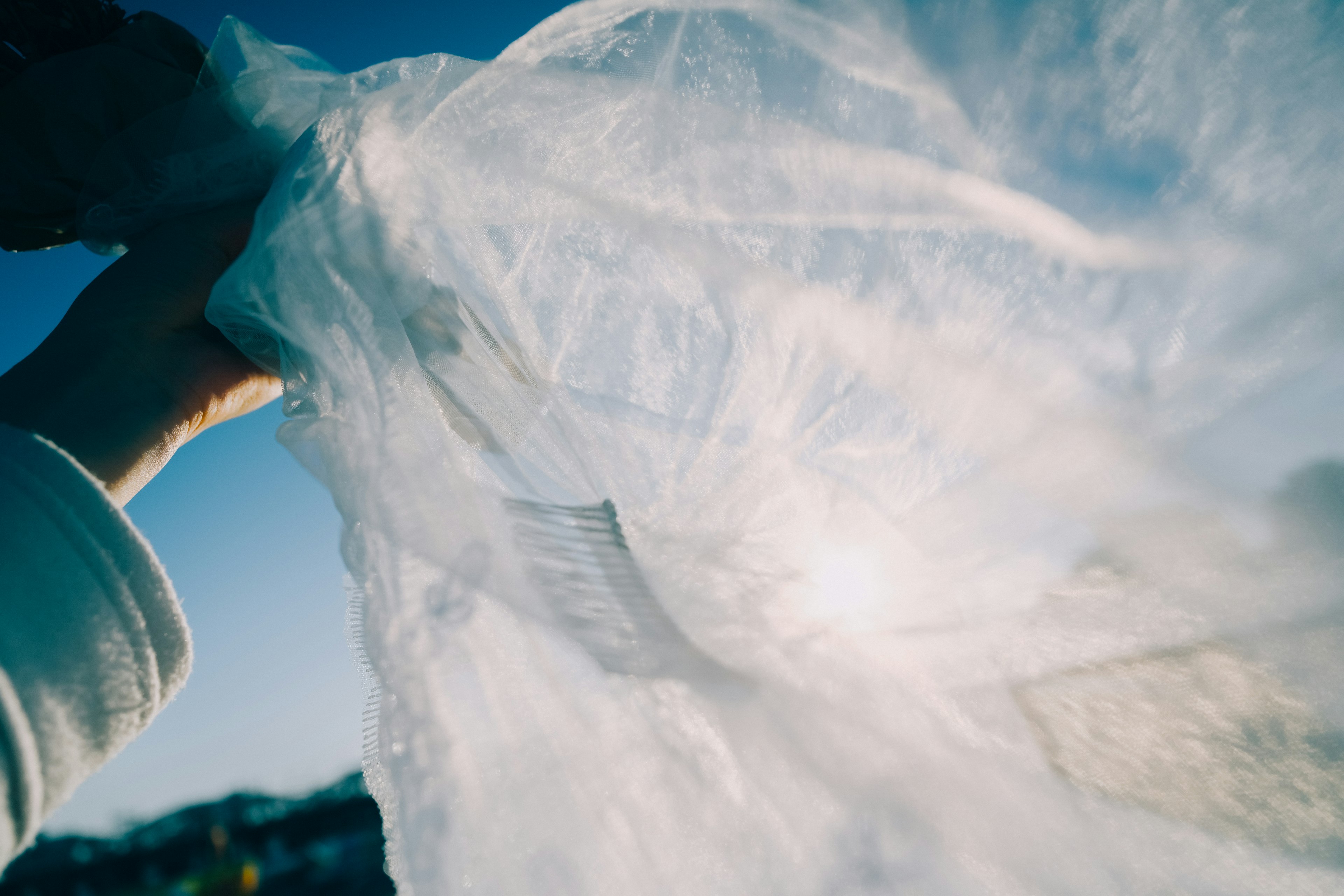 A hand holding a translucent fabric against a blue sky