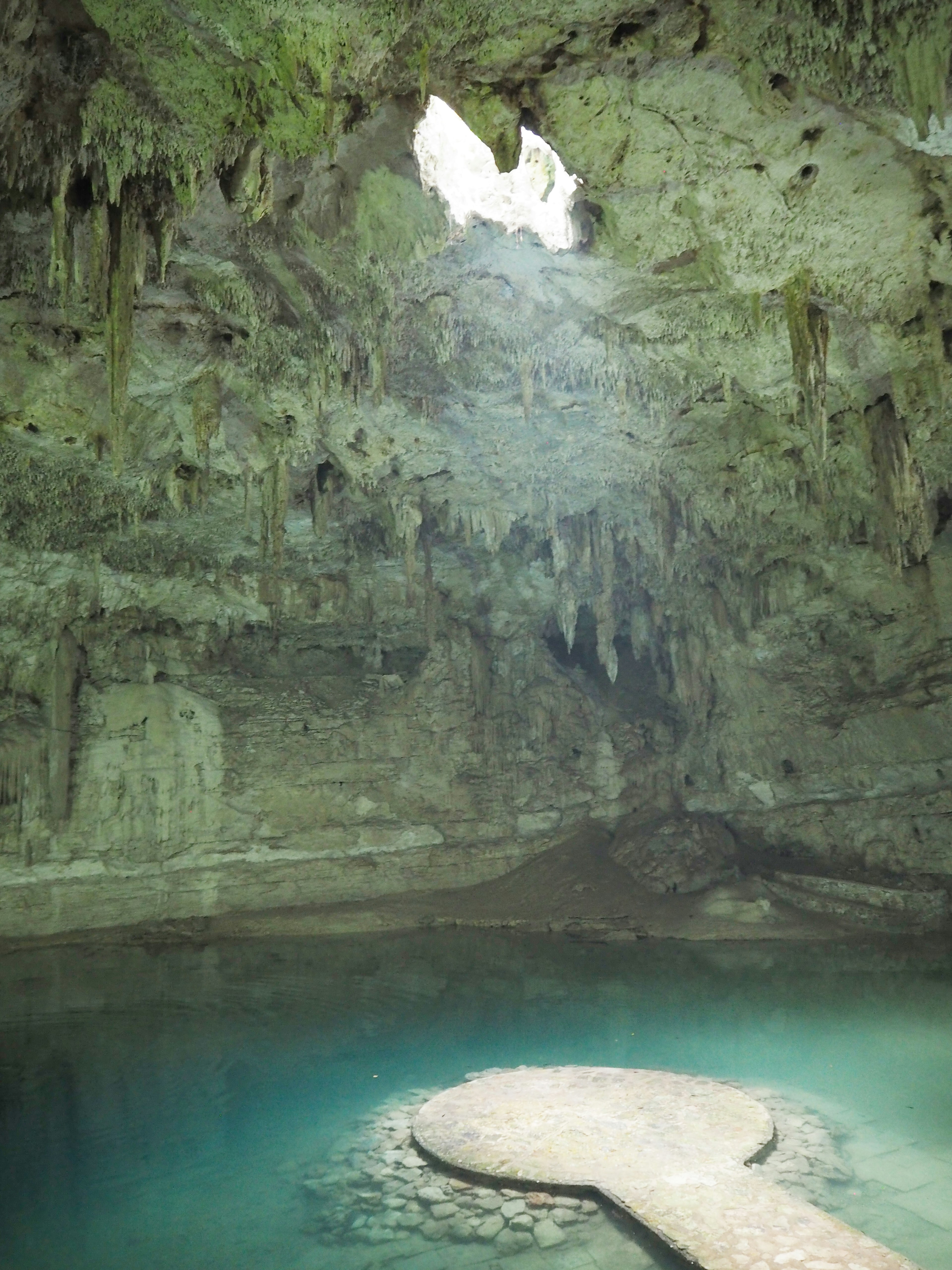 Interior de cueva misteriosa con piscina de agua azul y luz que entra