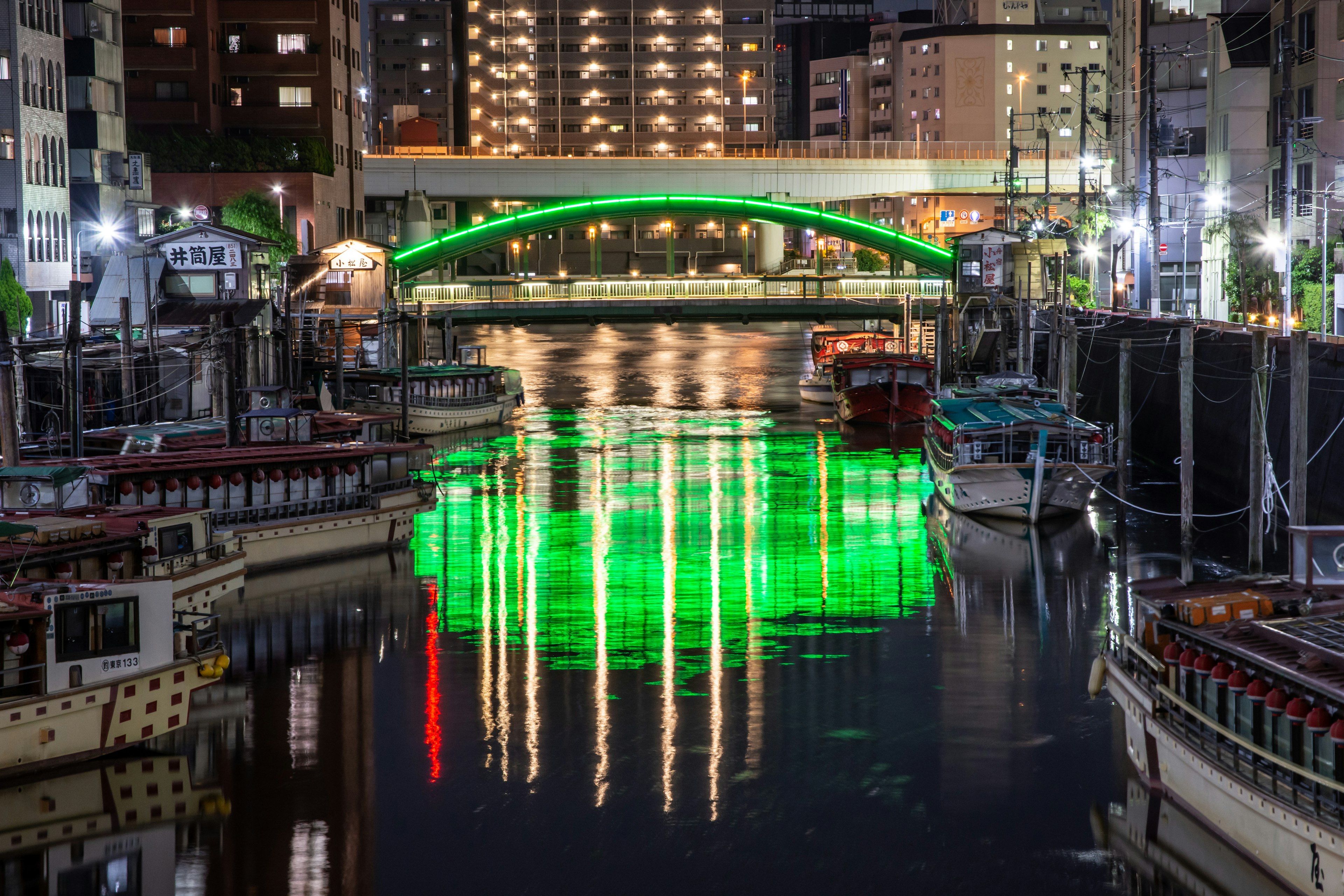 Vue nocturne d'un pont vert se reflétant sur la rivière avec des bateaux