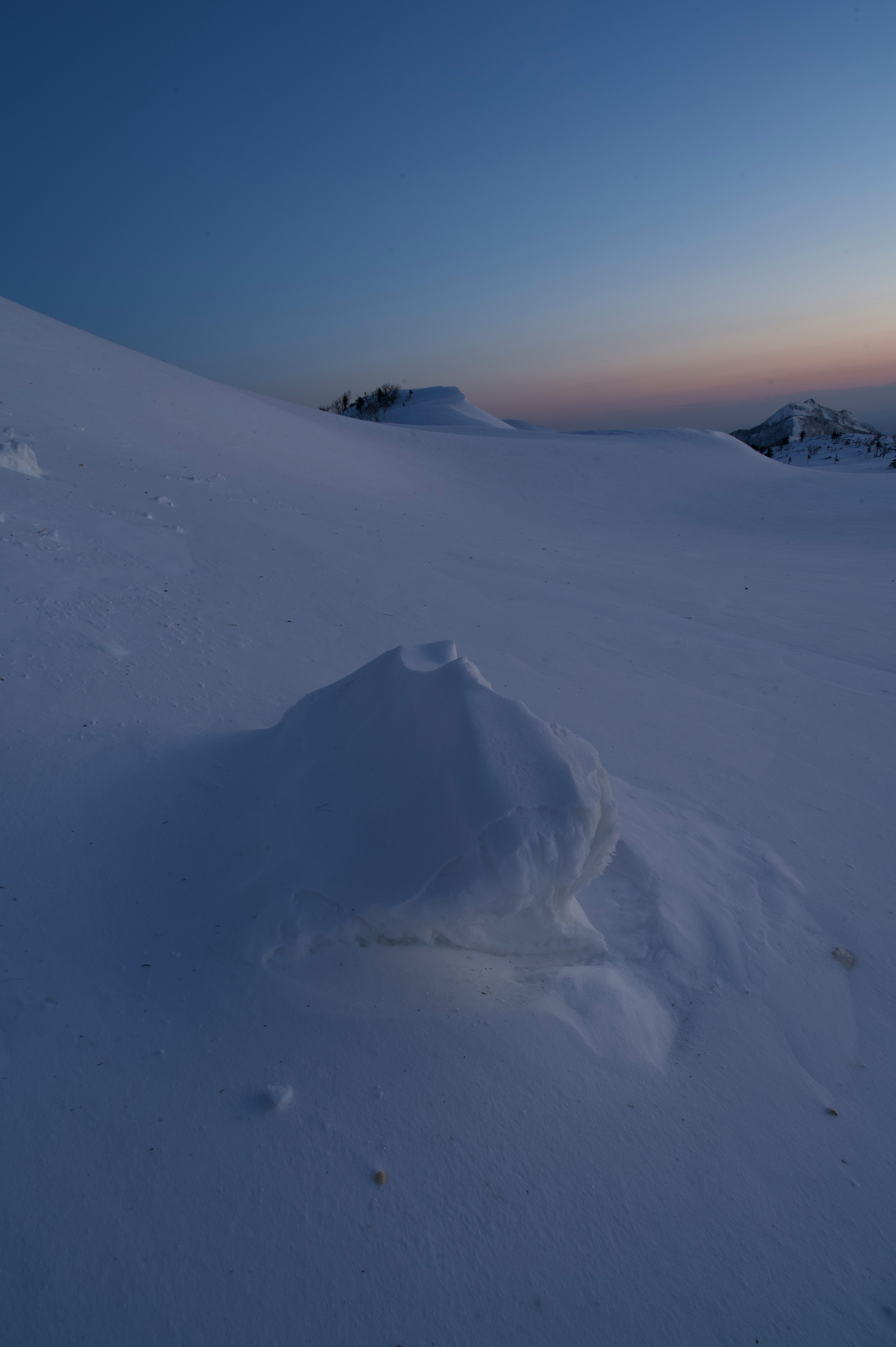 雪に覆われた風景の中に小さな雪山と薄暗い空