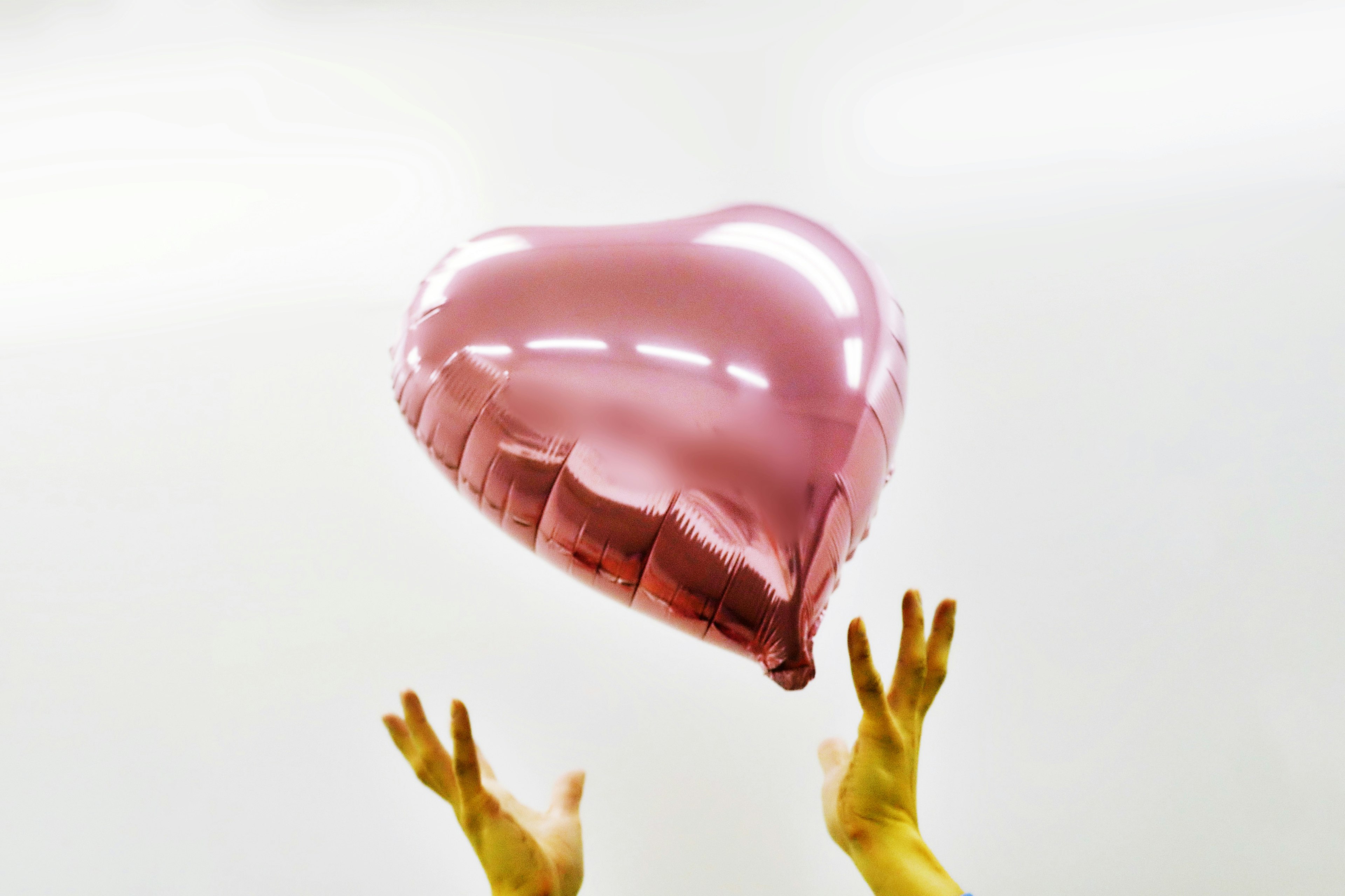 Tangan mengangkat balon berbentuk hati berwarna pink