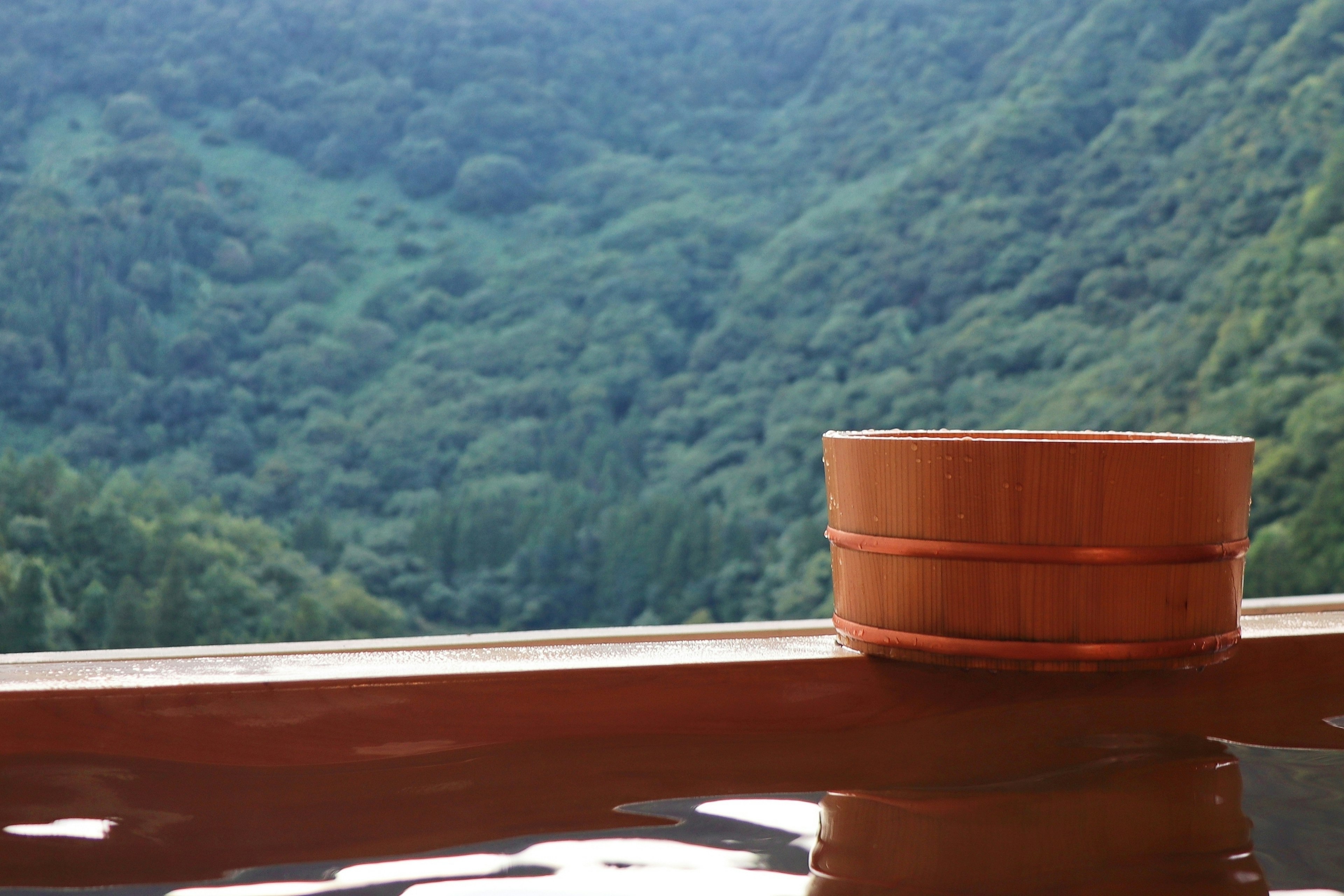 Szene mit einer Holzbadewanne und einem Eimer, mit grünen Bergen im Hintergrund