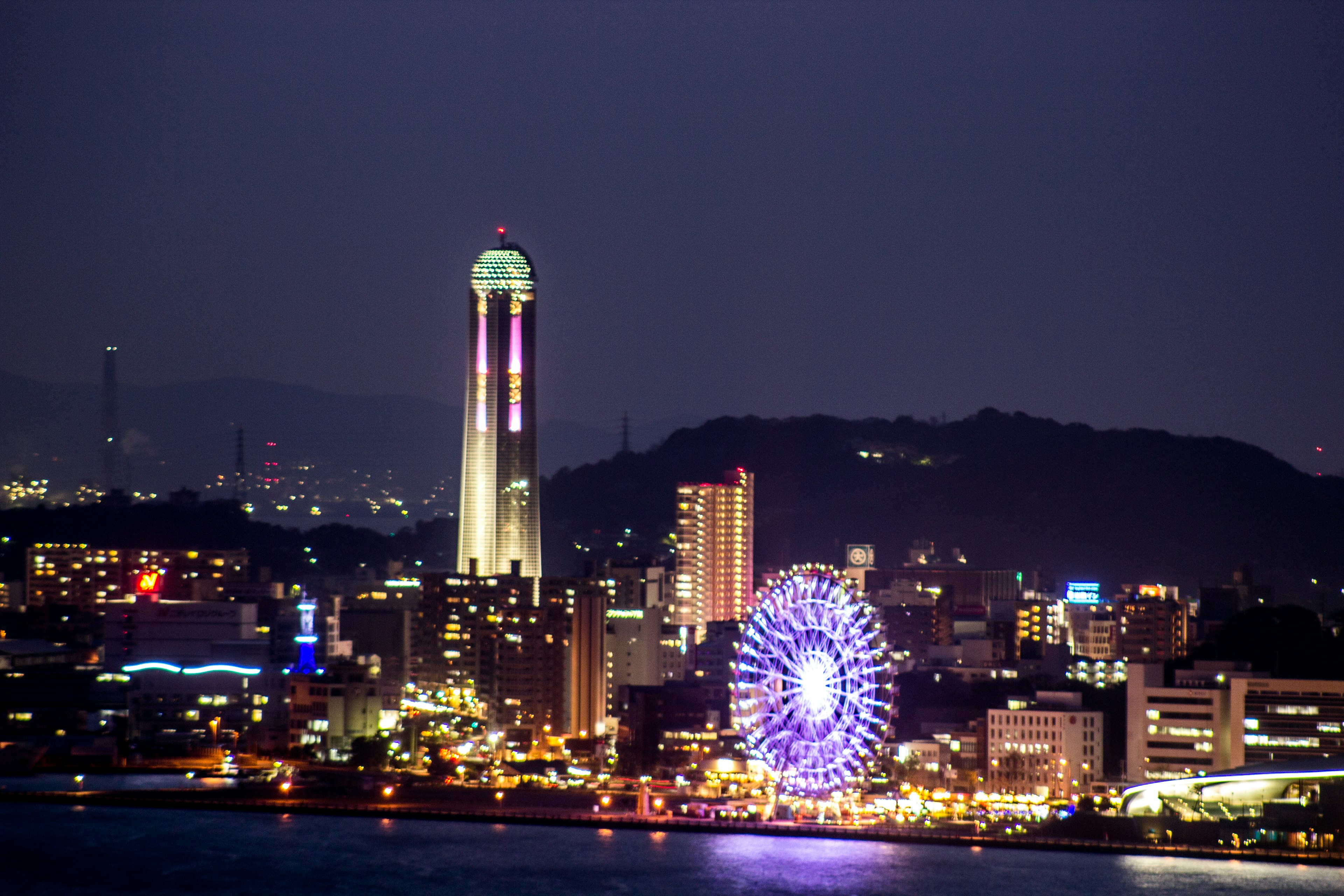 City skyline illuminated at night featuring a tower and a ferris wheel