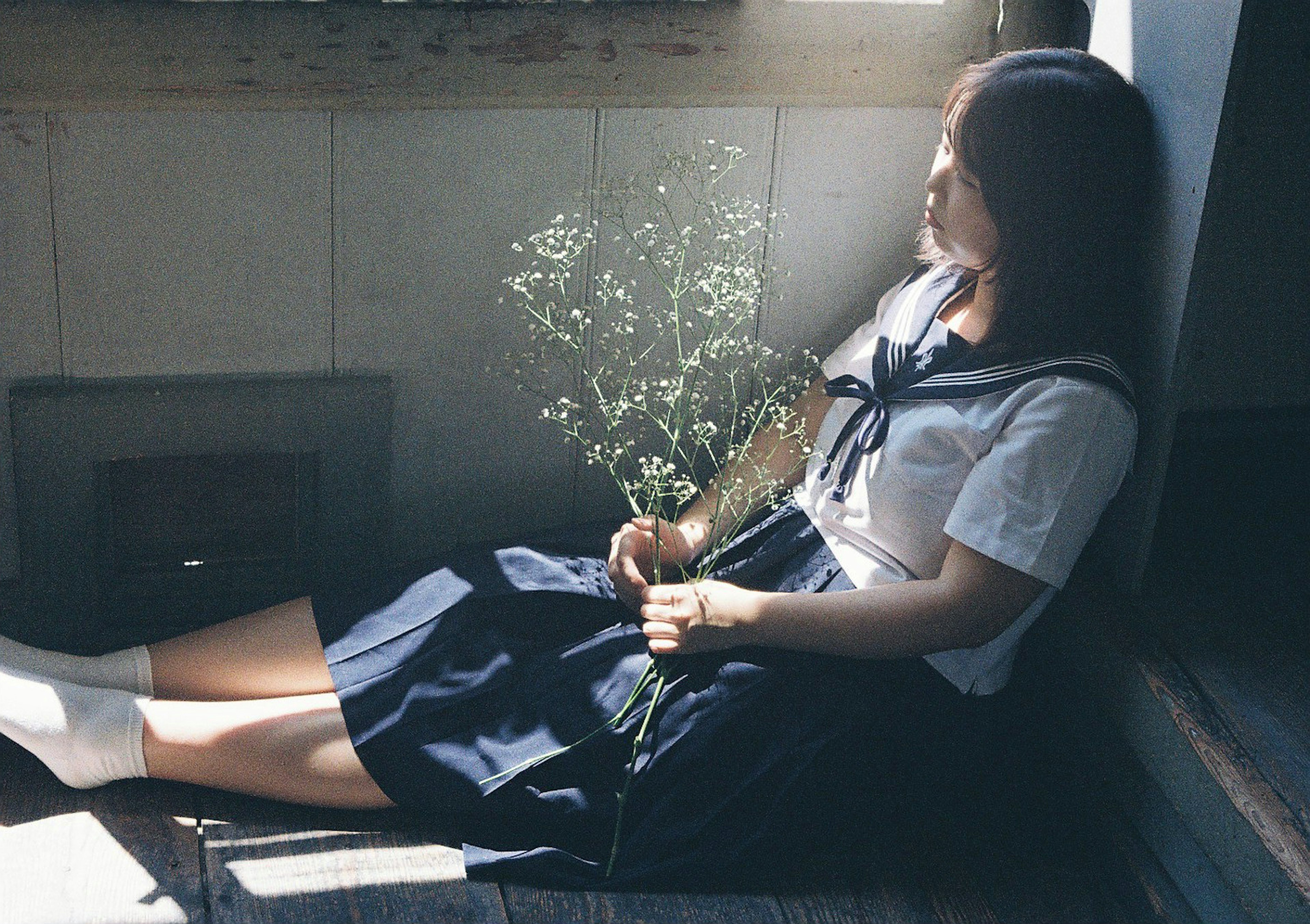 Una chica en uniforme escolar sentada tranquilamente junto a una ventana sosteniendo un ramo