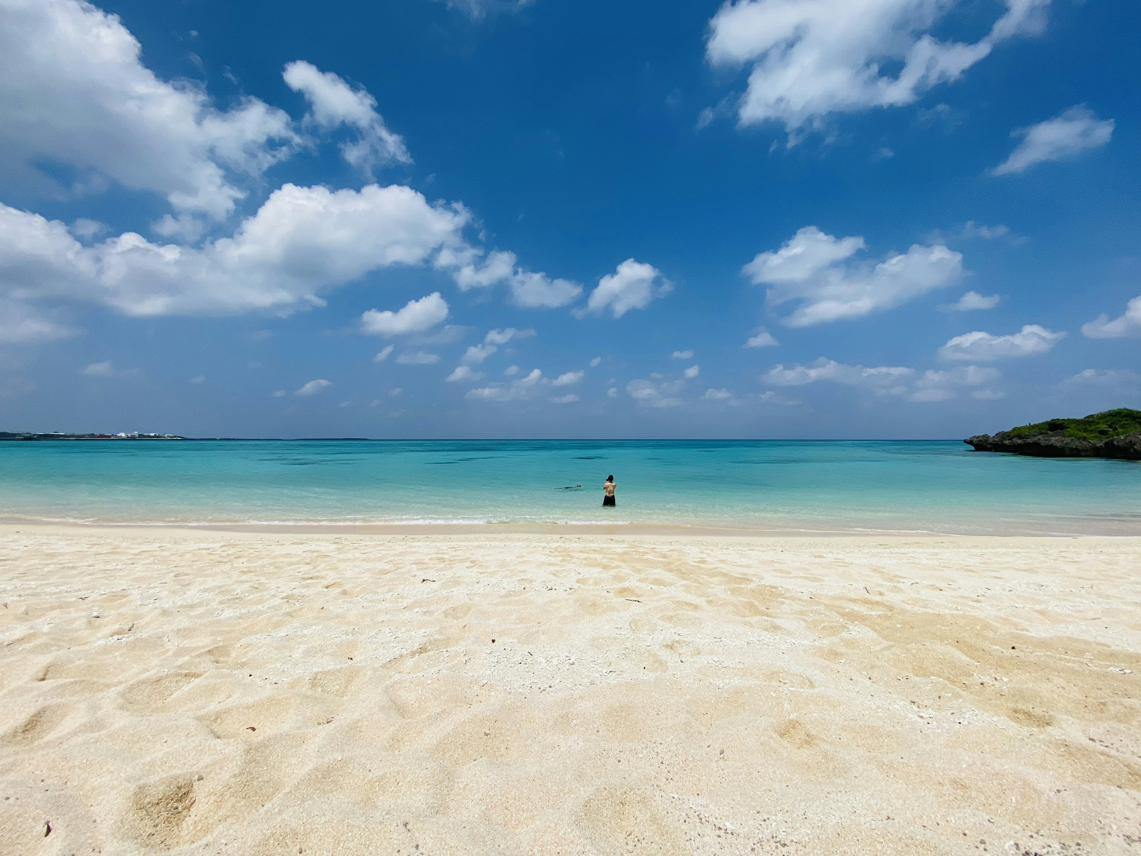 A person standing on a beach with blue sea and white sand