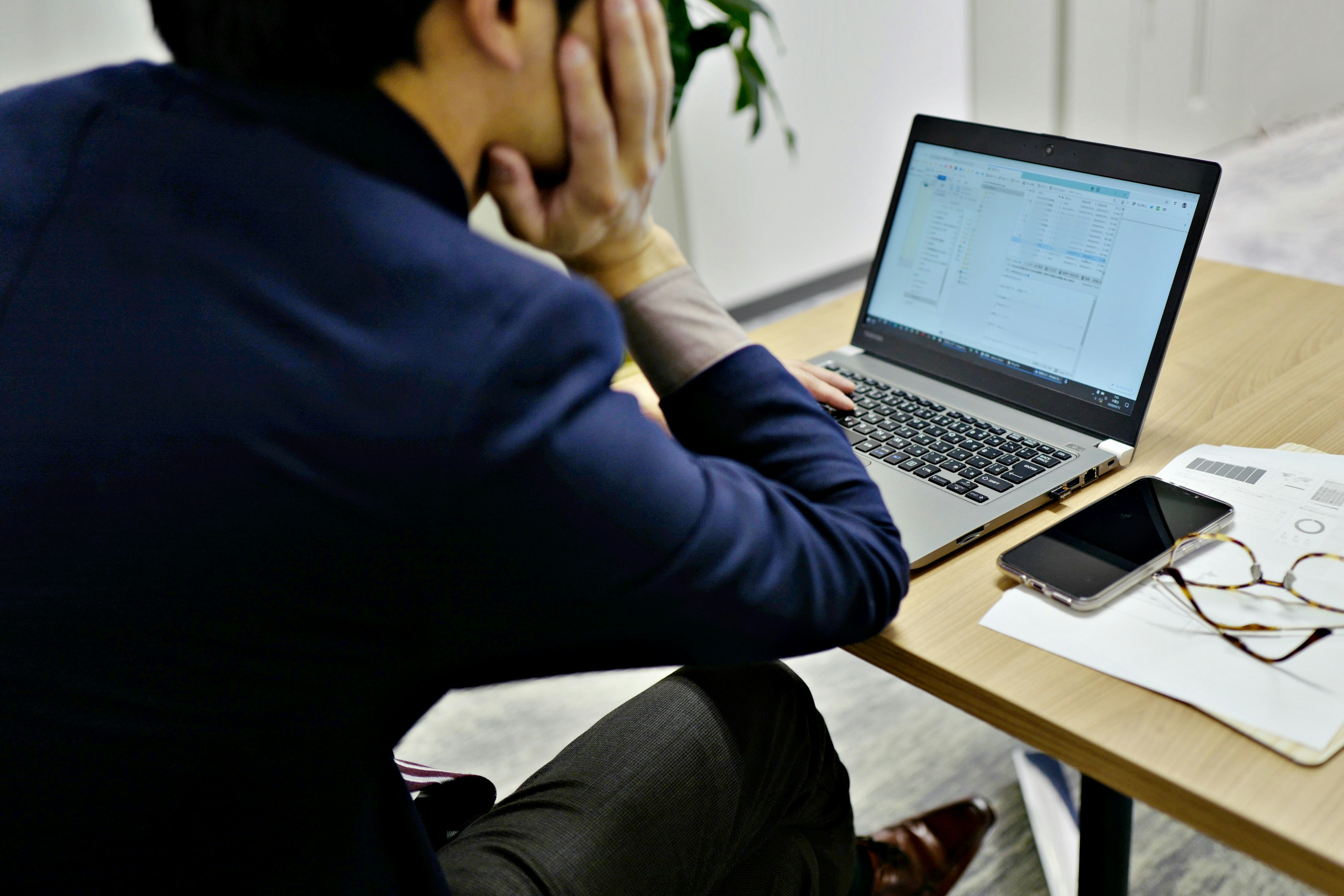 A man sitting at a desk looking at a laptop with his hand on his face