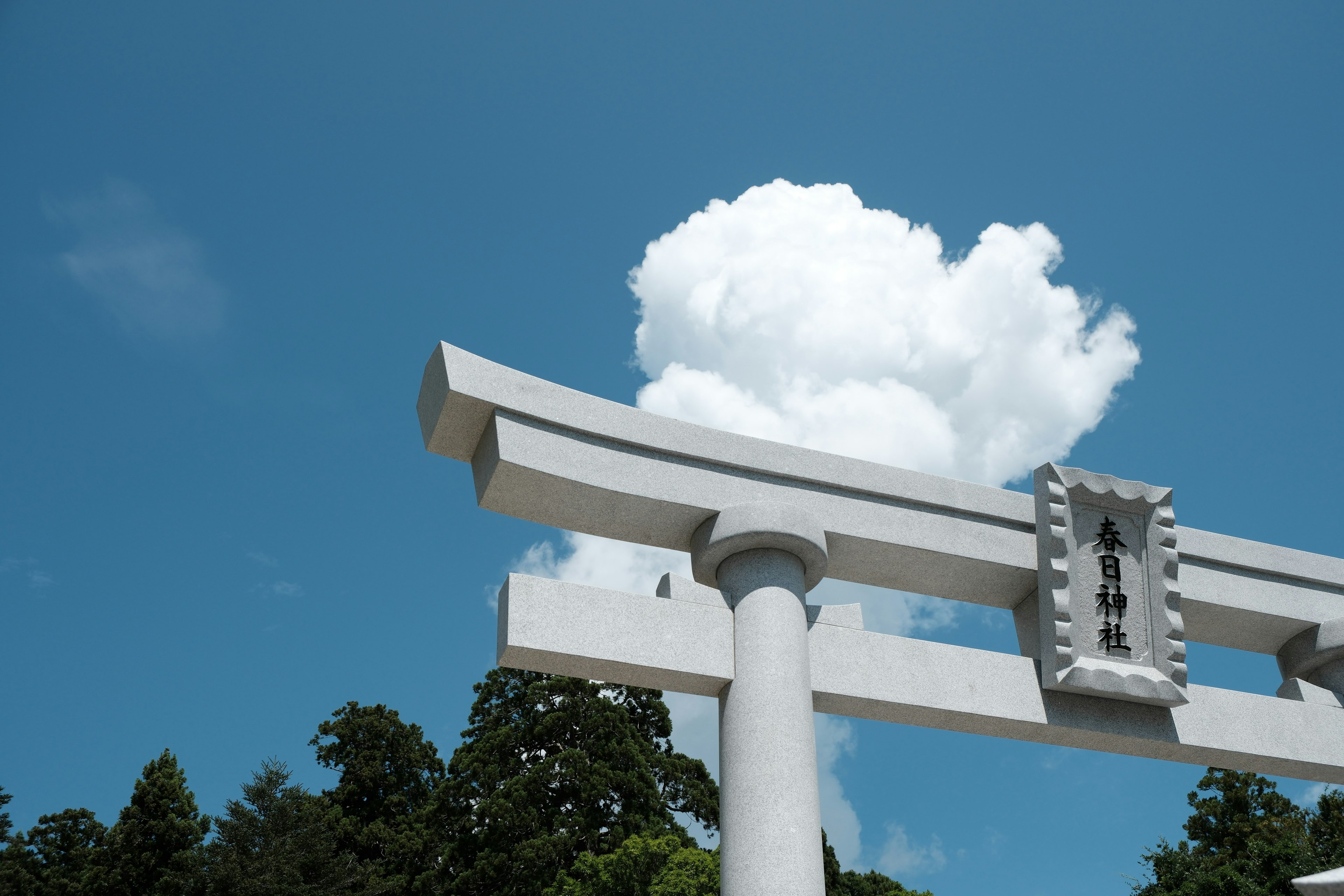 White torii gate under a blue sky with a fluffy white cloud