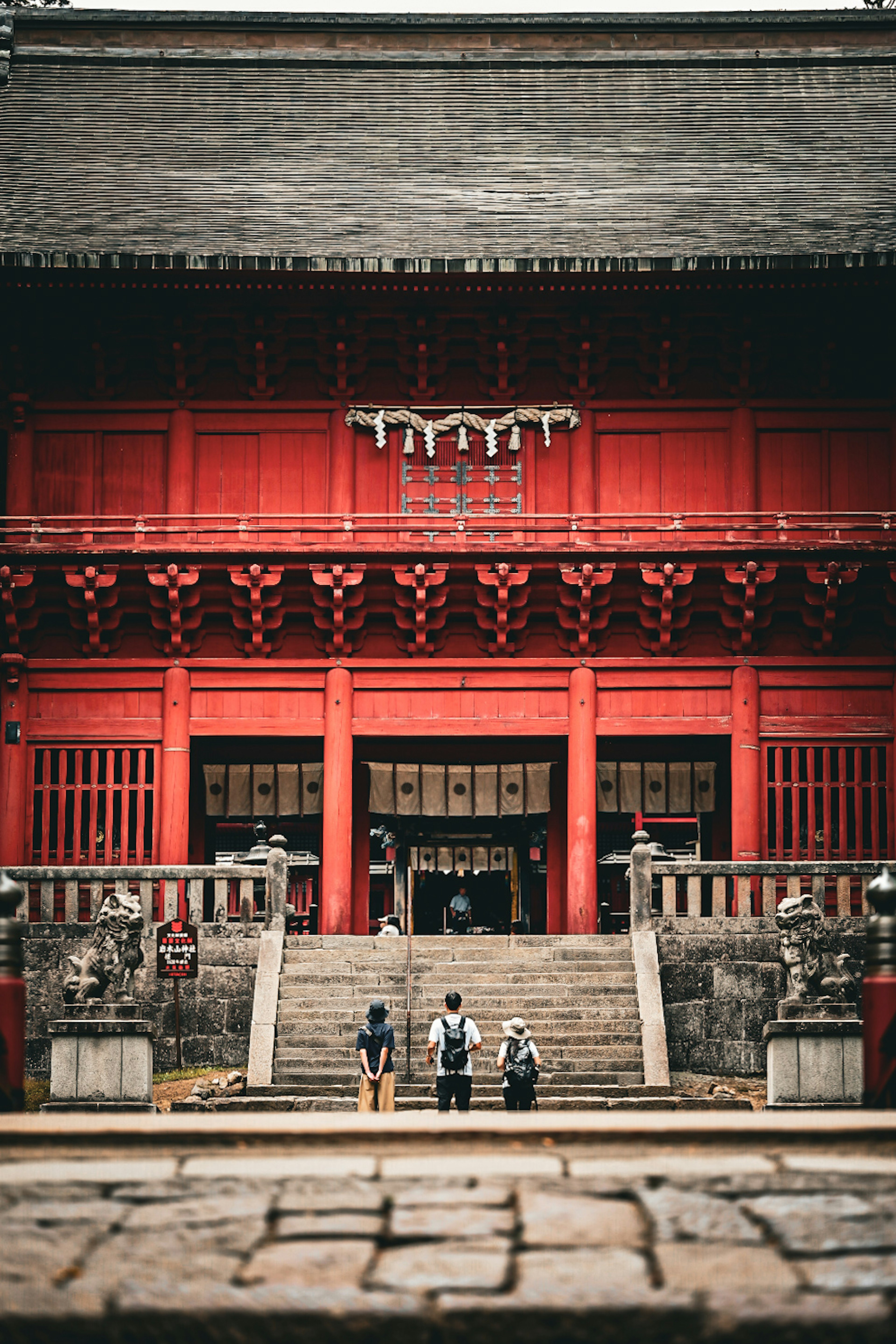 People standing in front of a red temple with stone lion statues flanking the entrance