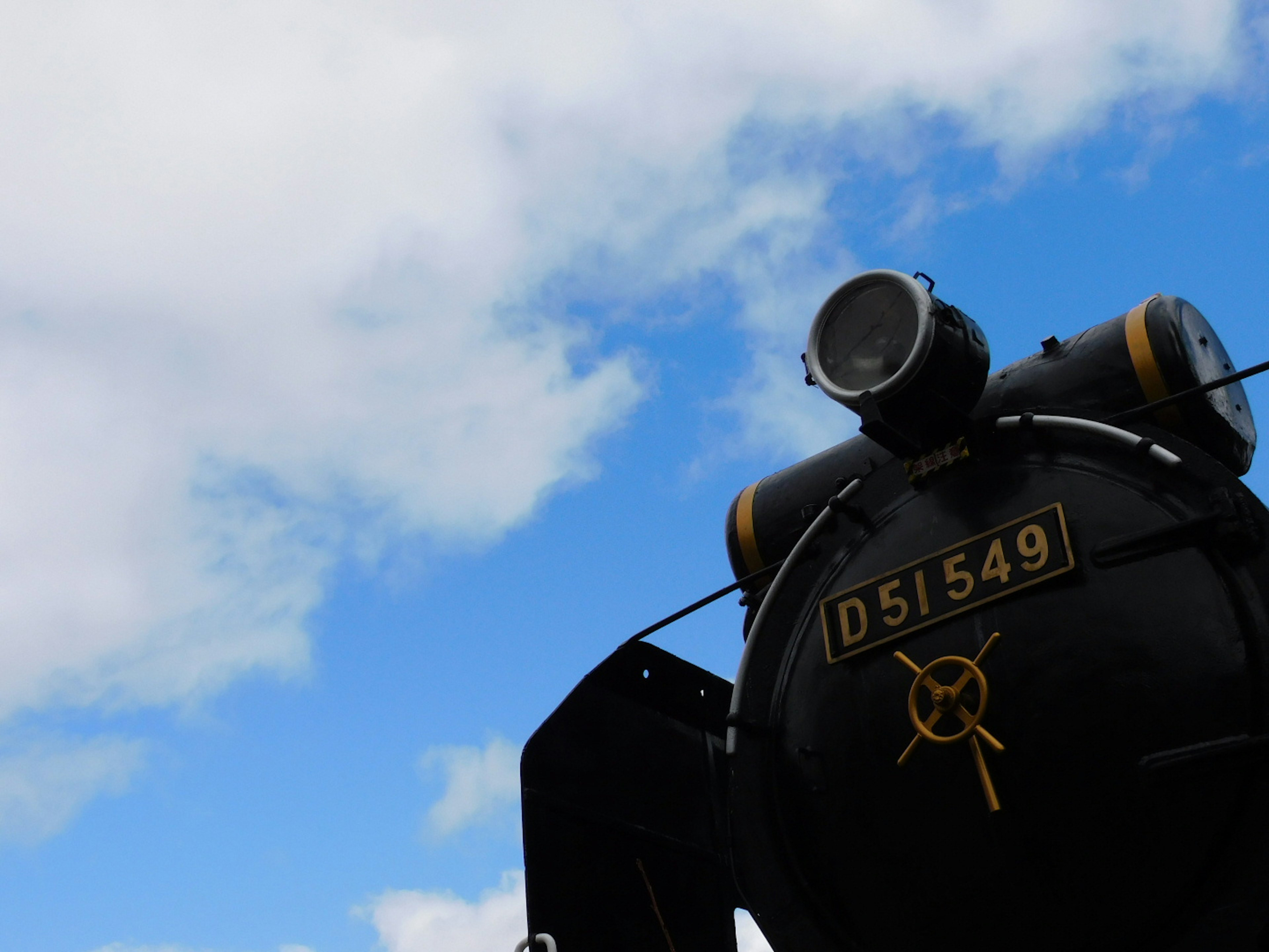 Locomotora de vapor negra con el número D51549 contra un cielo azul