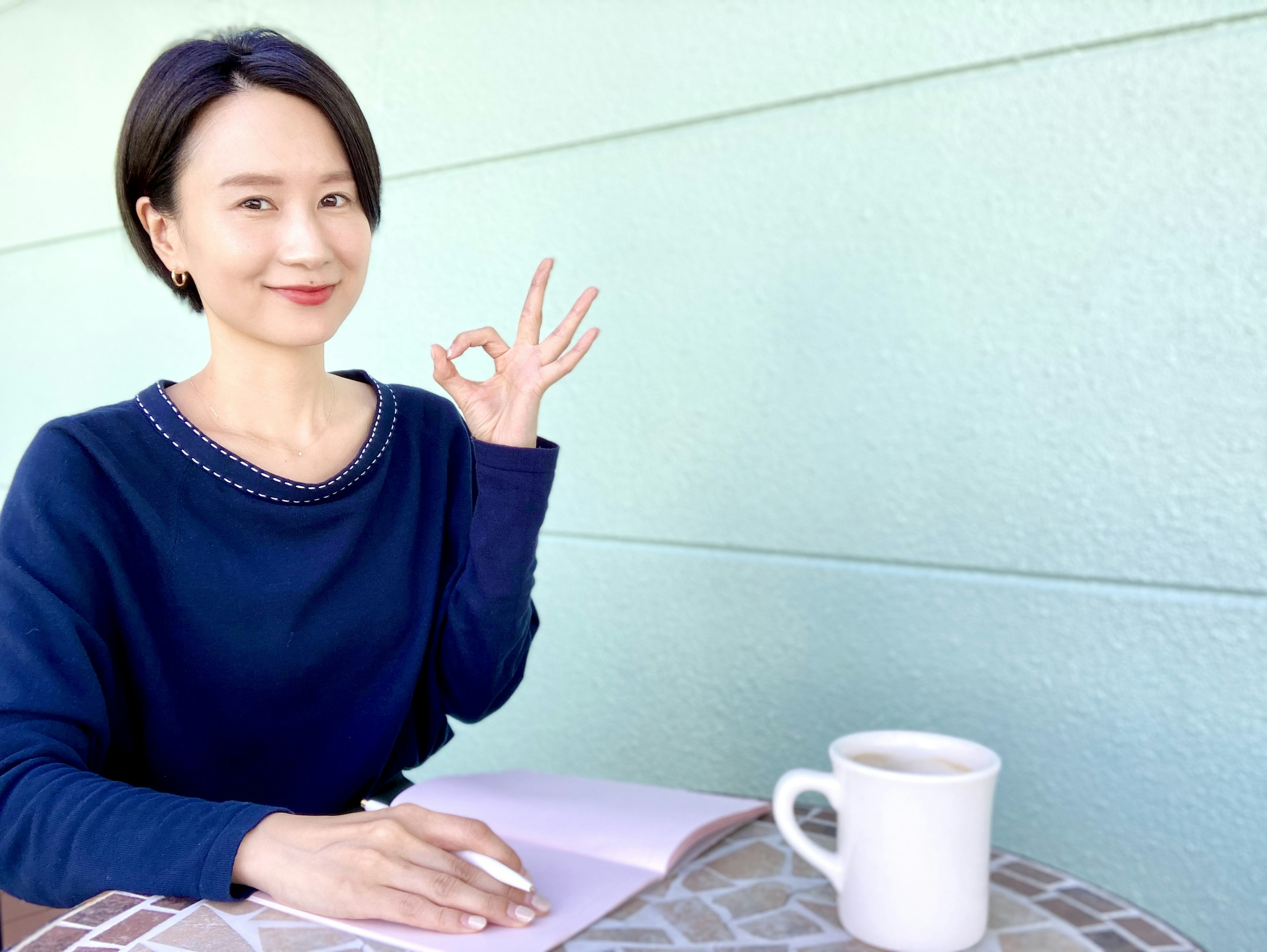 Une femme en pull bleu souriante faisant un signe OK de la main